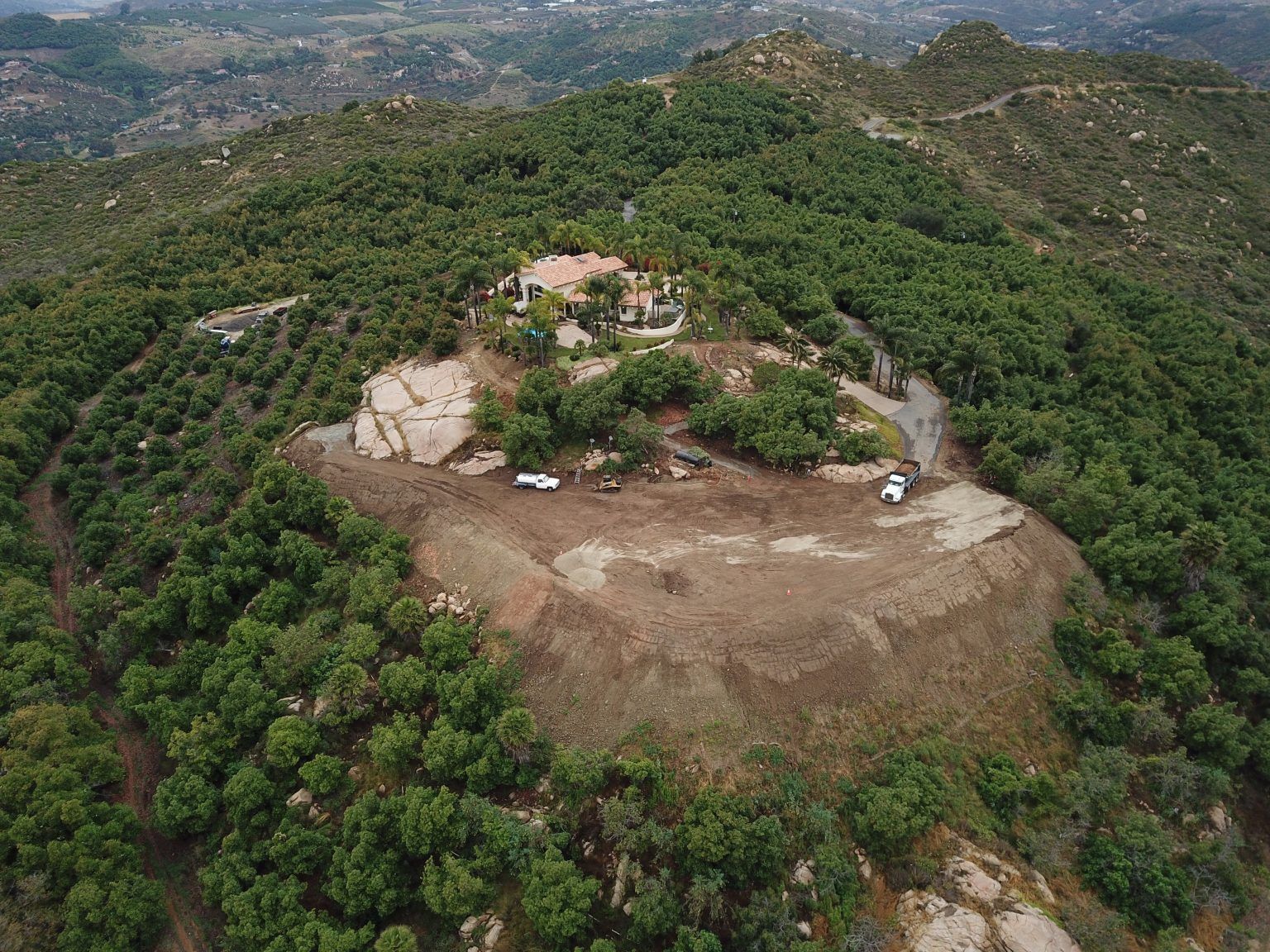 Aerial view of a rocky hilltop clearing surrounded by dense green forest and distant mountains