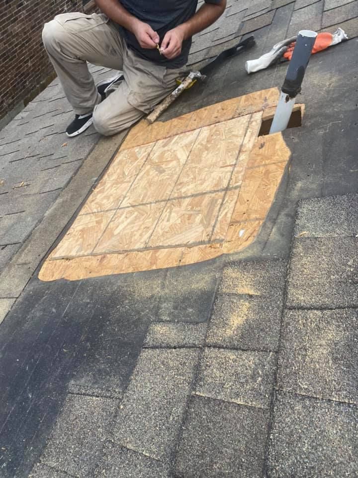 Person kneeling on a roof, replacing a section of plywood with a saw and tools visible.