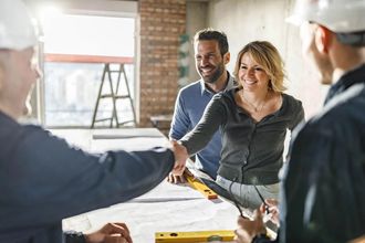 Couple shaking hands with construction workers in a building, smiling.