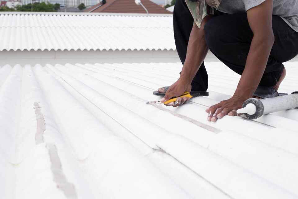 Person on a white roof, applying sealant.