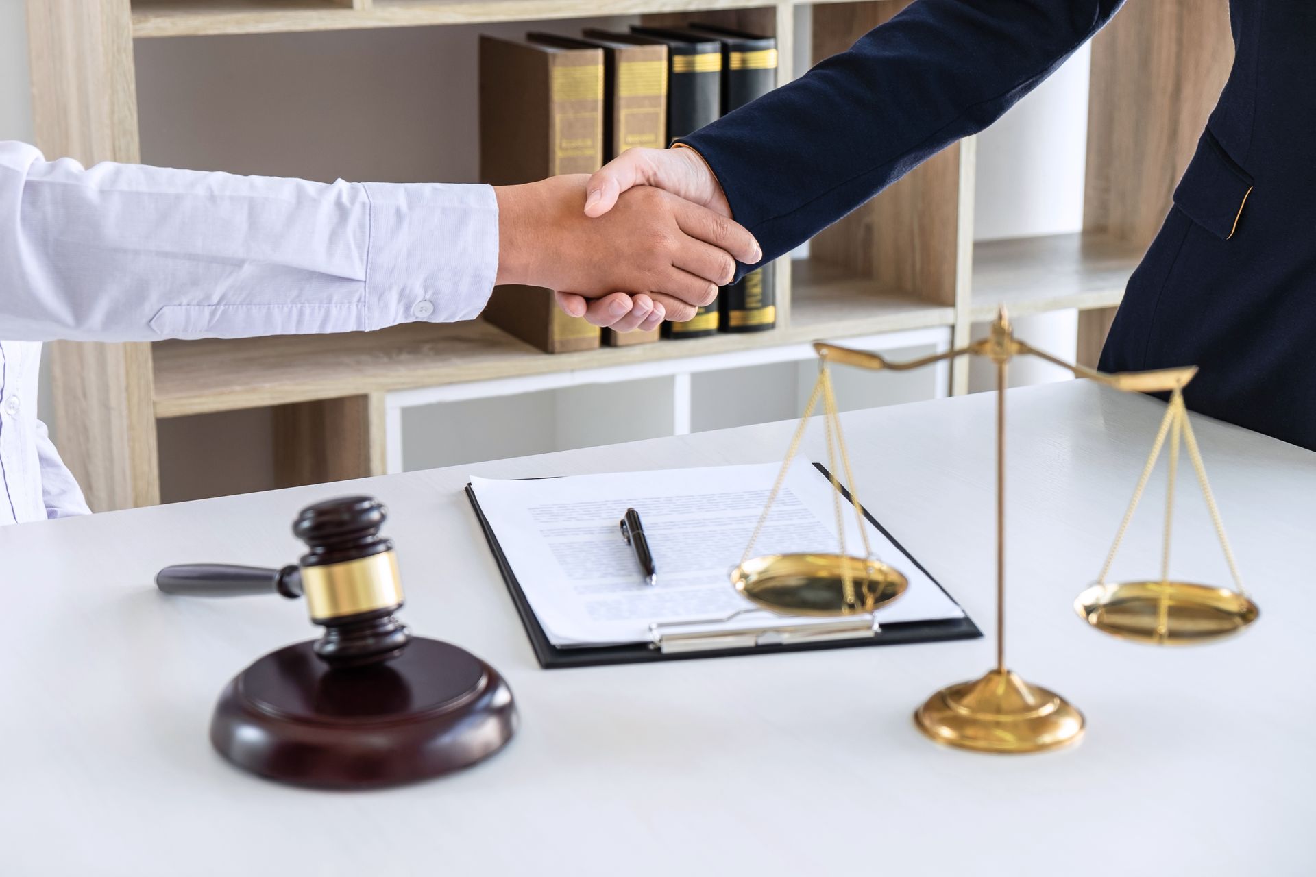 Handshake of a client and a lawyer over a document. The table has a gavel and a scale of justice. Handshake of a client and a lawyer over a document. The table has a gavel and a scale of justice.