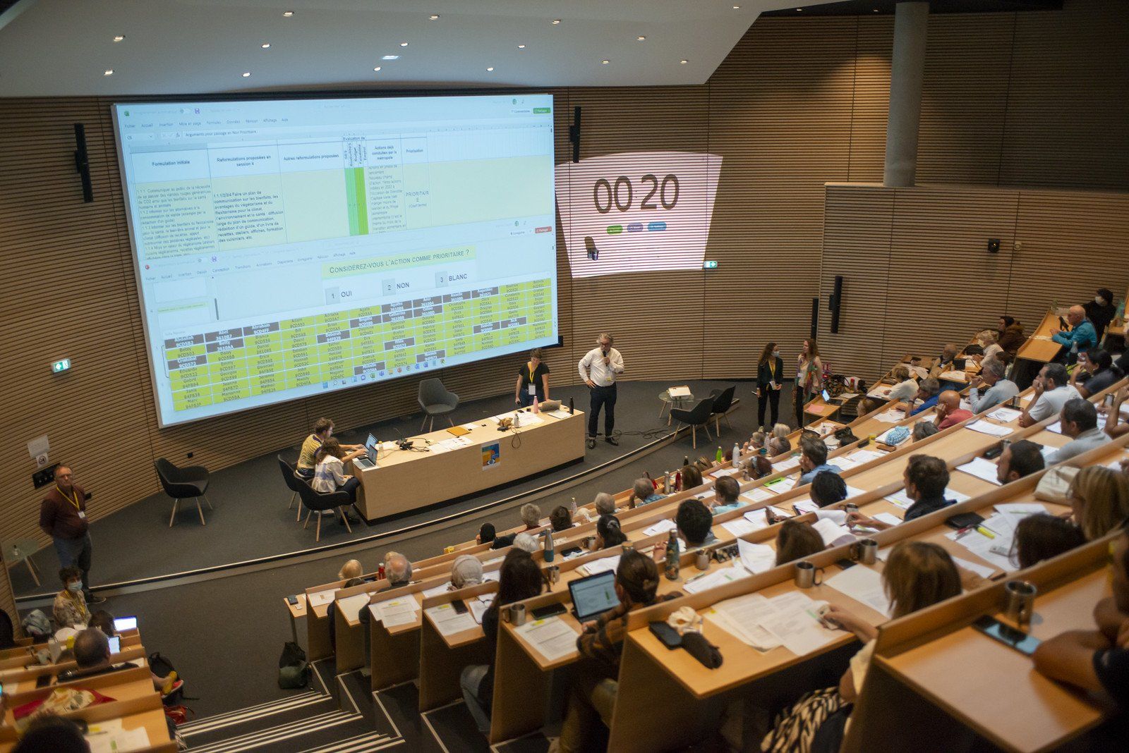Un grand groupe de personnes est assise dans un auditorium et regarde une présentation.