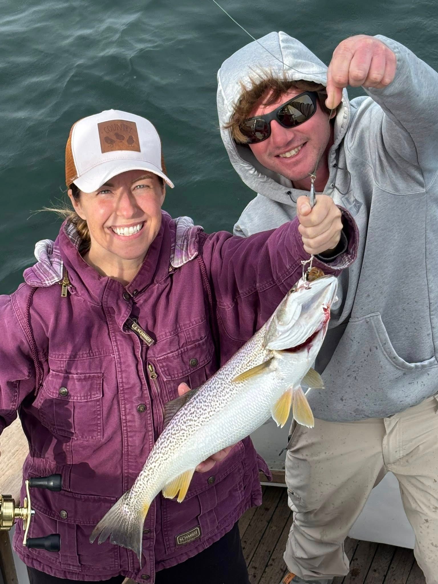Two people smiling on a boat, holding a large fish over the water.