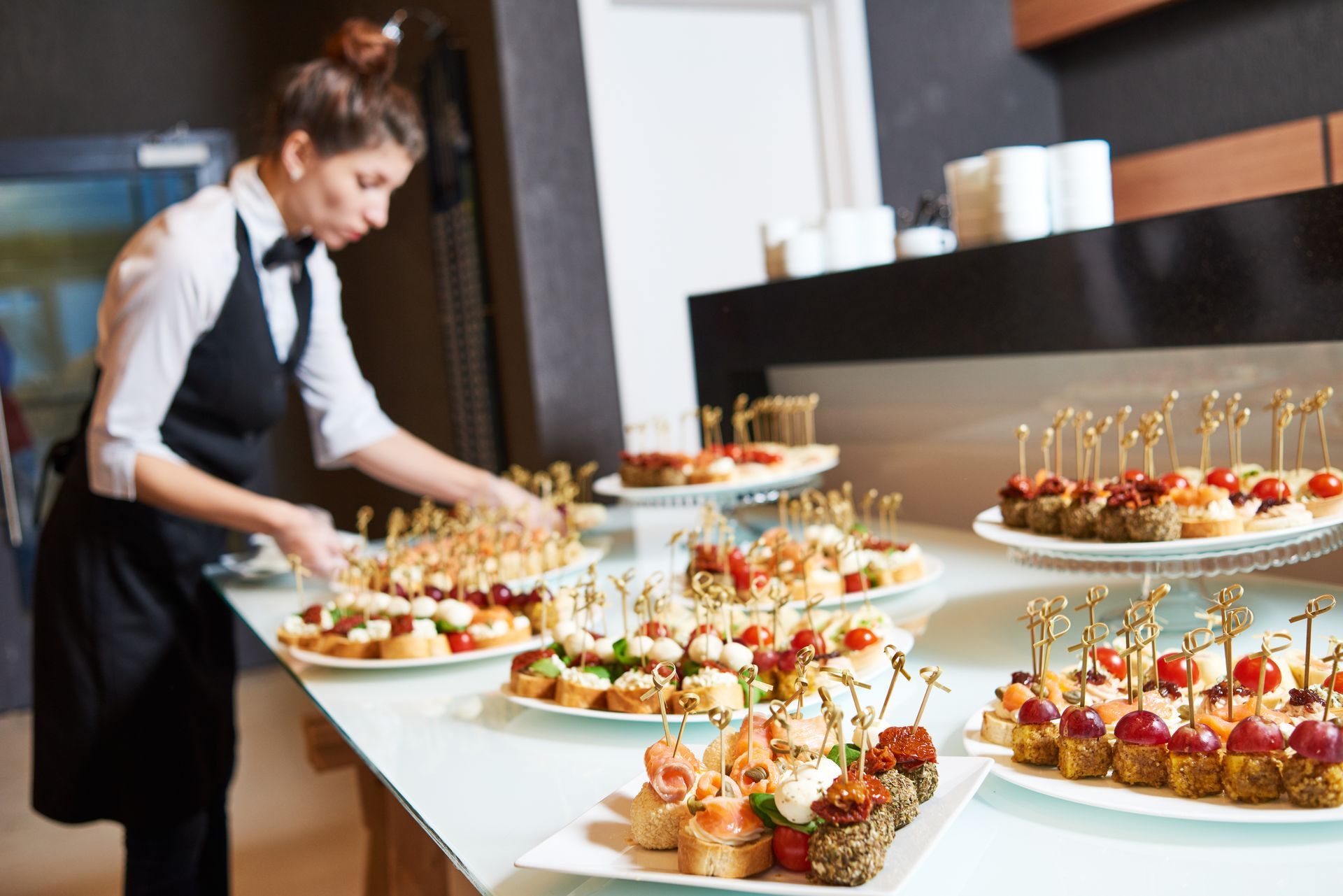 Caterer arranging elegant bite-size desserts on white tables at a buffet setup