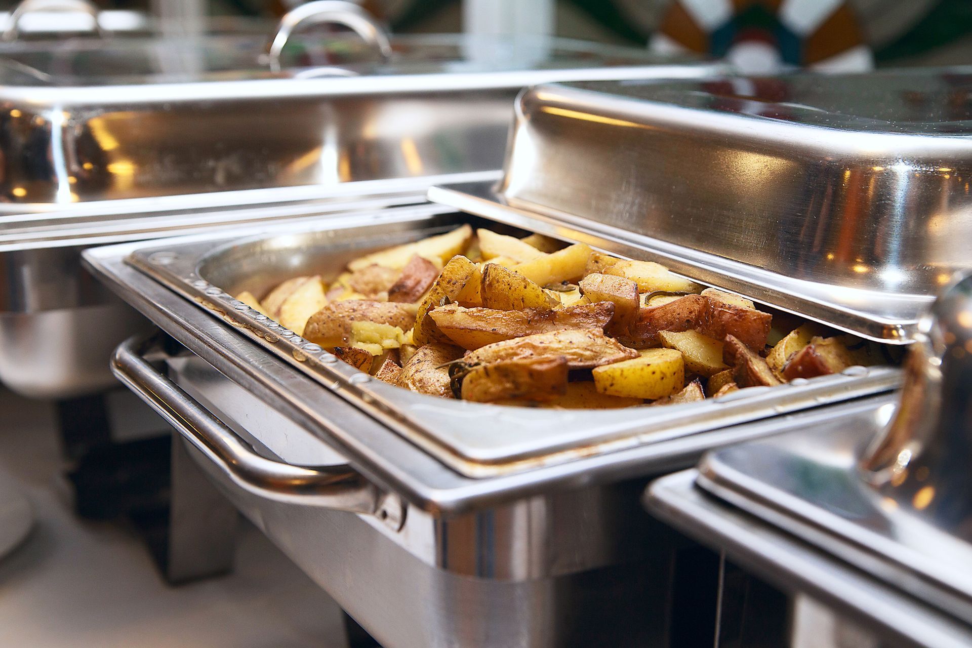 Tray of roasted potatoes and meat in a stainless steel buffet warmer