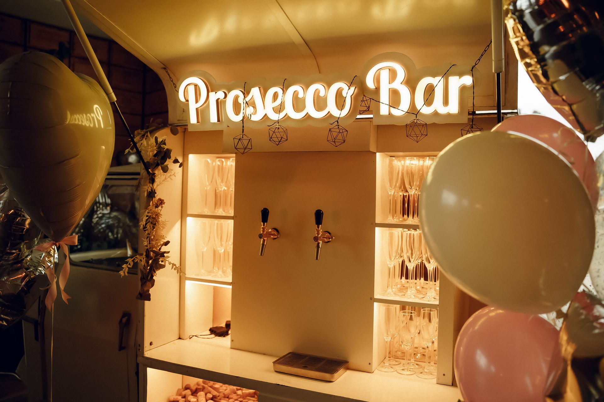 Prosecco bar with glowing sign, balloons, and a decorated champagne station indoors