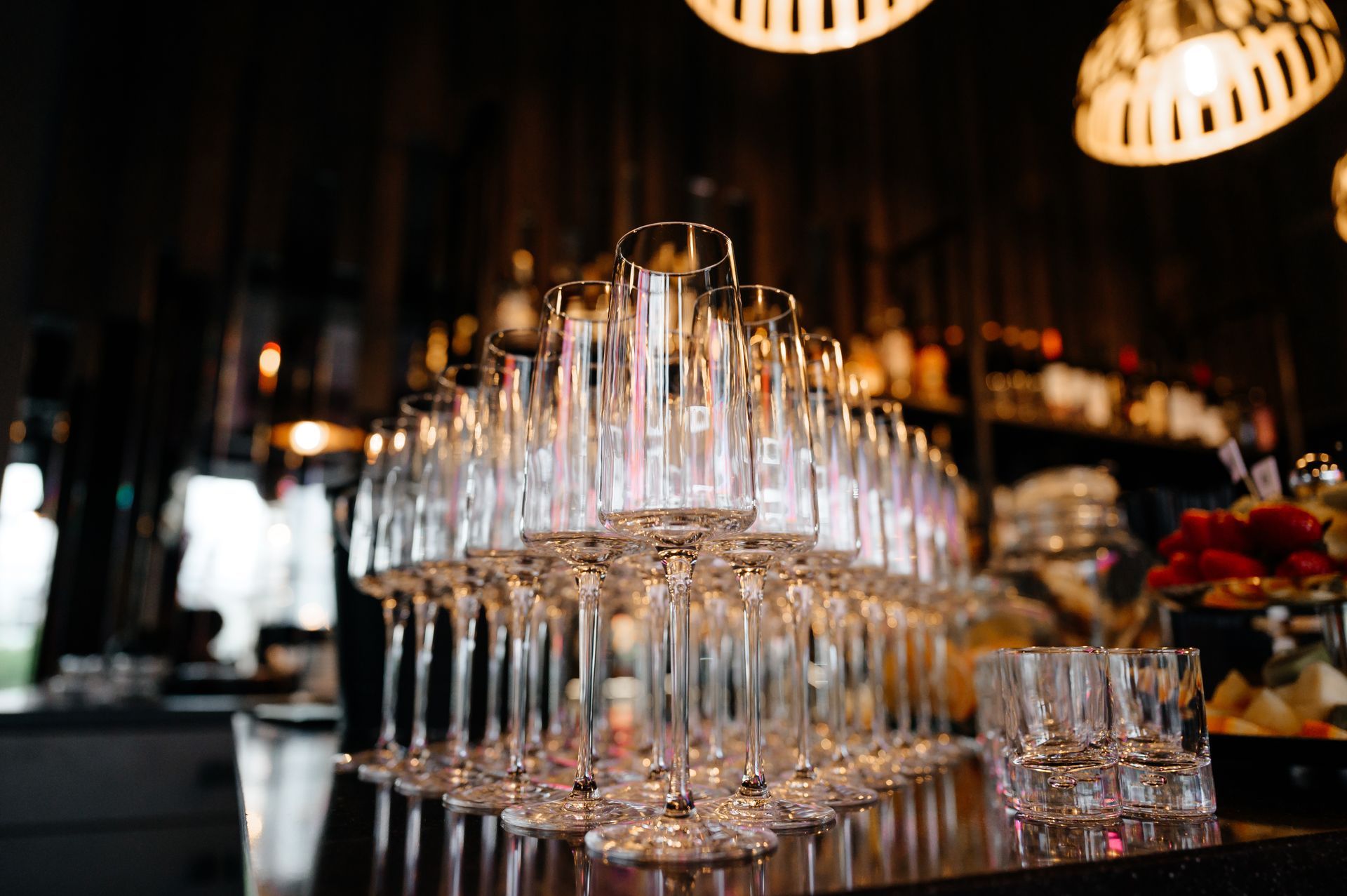 Rows of empty champagne flutes on a dimly lit bar counter, with warm hanging lights above