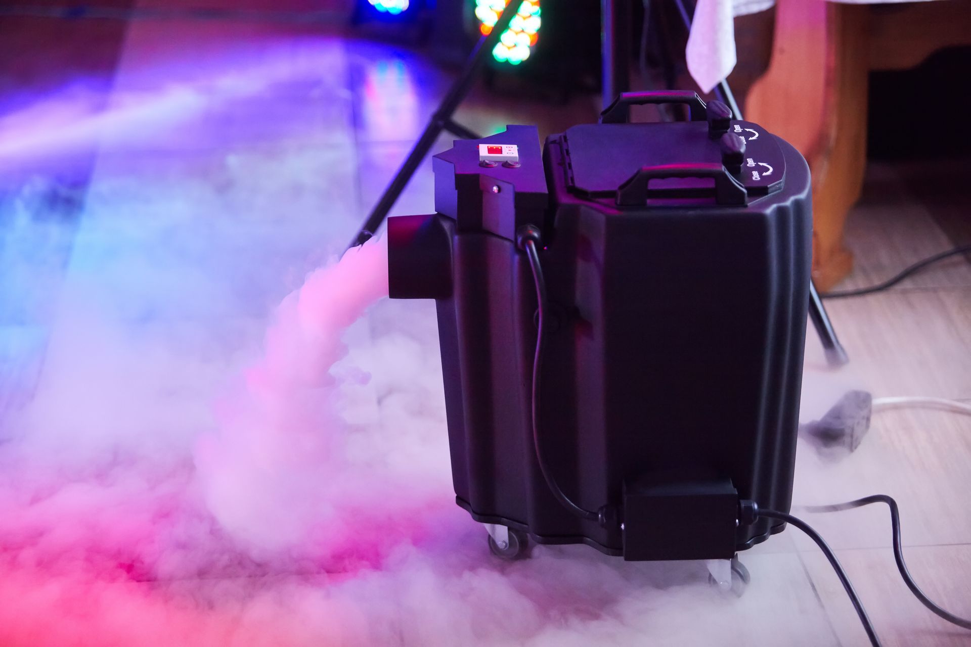 Black fog machine on a stage floor, blowing white smoke under purple lighting