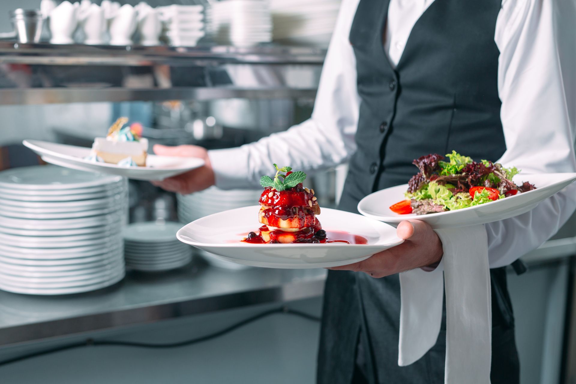Waiter carrying plated gourmet dishes in a restaurant kitchen