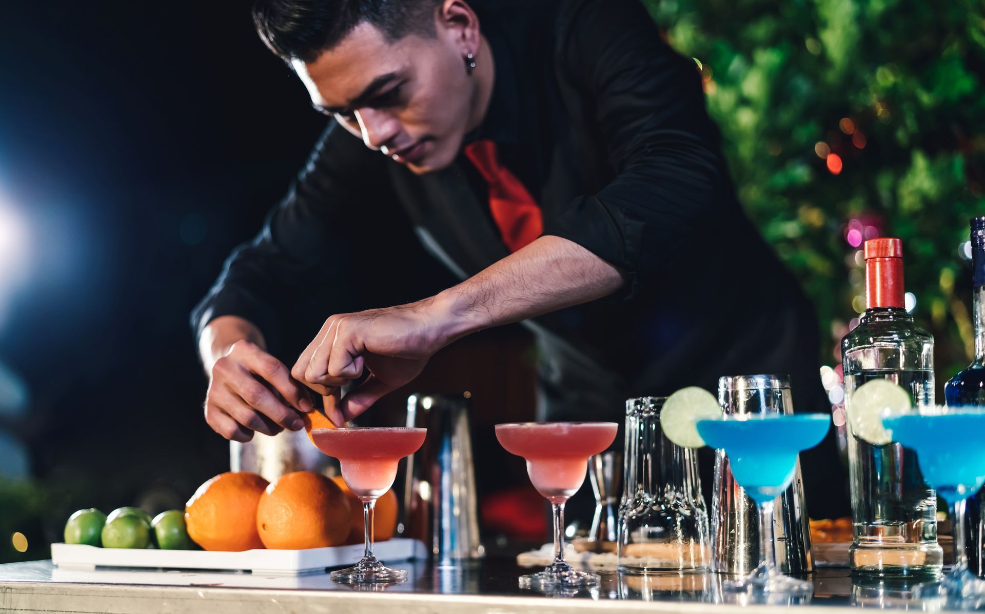 Bartender mixing colorful cocktails at a bar with fruit and bottles on the counter