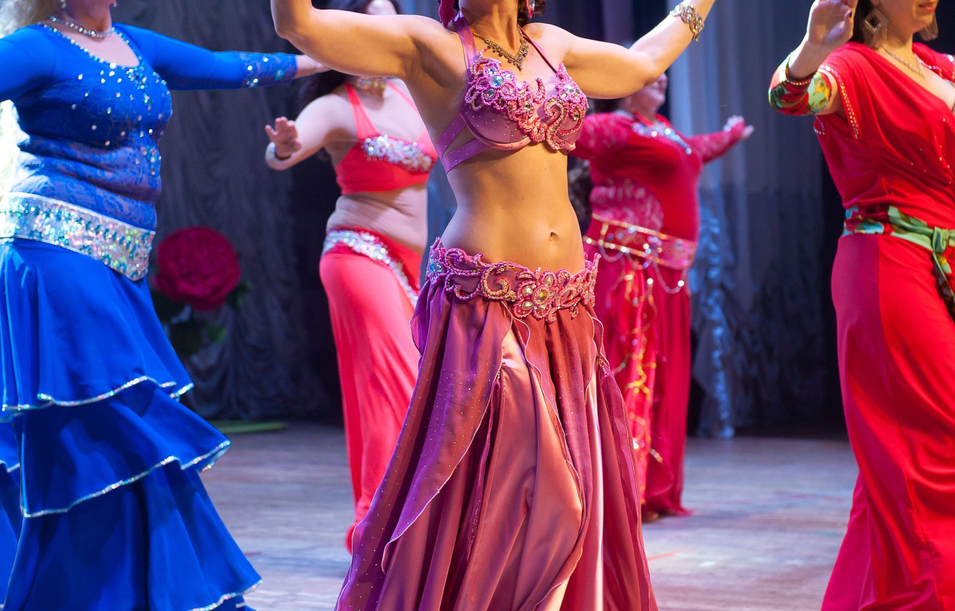 Colorful belly dancers in bright pink, blue, and red costumes performing on stage