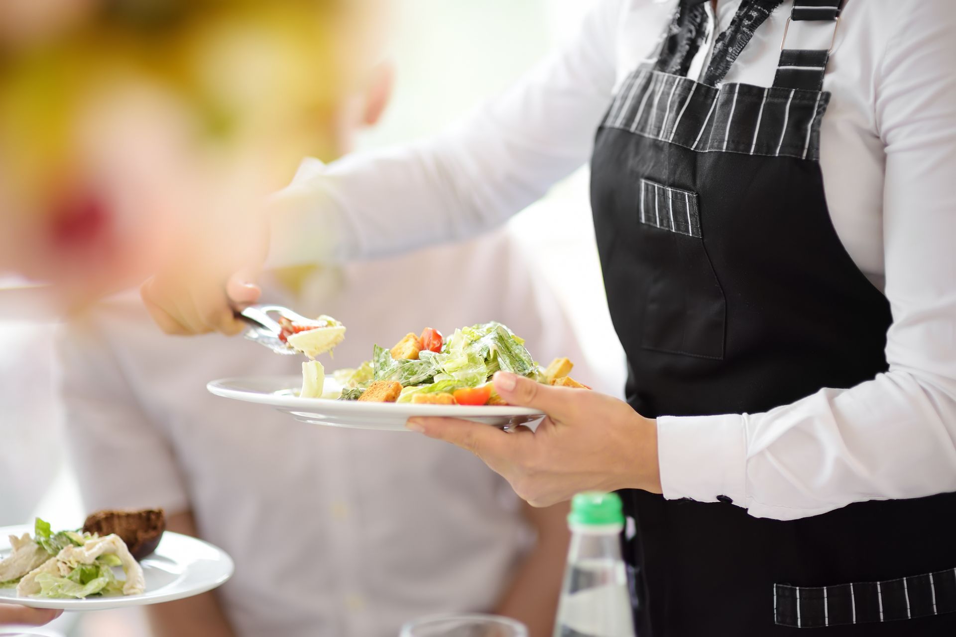 Server holding a plate of salad at a buffet, with a blurred dining background
