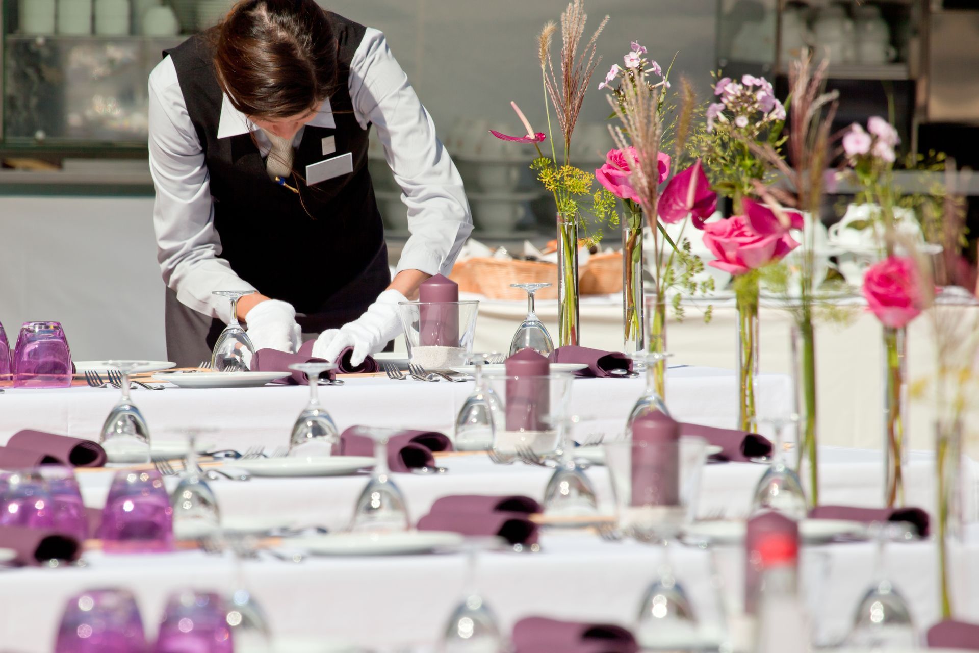 Event staff setting a table with pink floral centerpieces and white linens in a bright venue
