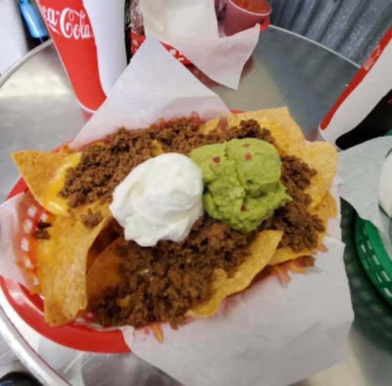 Nachos with ground meat, cheese, sour cream, and guacamole in a basket.