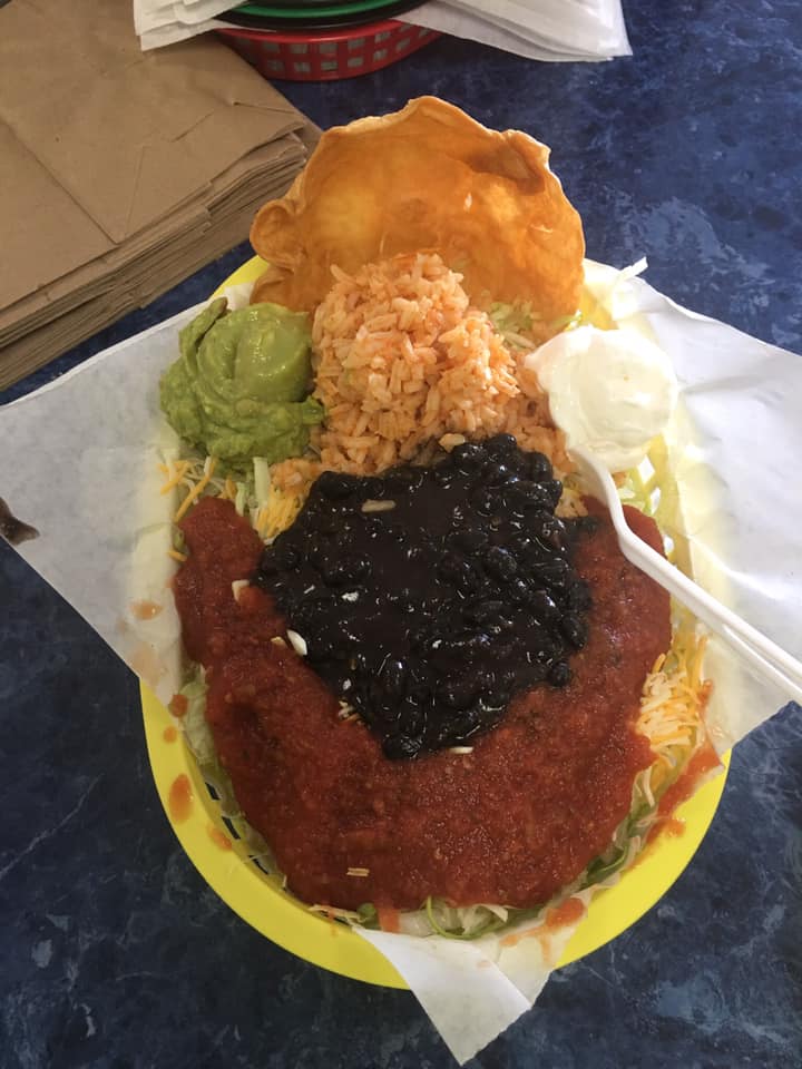 Yellow basket with Mexican food: red sauce, black beans, rice, guacamole, sour cream, and a fried tortilla.