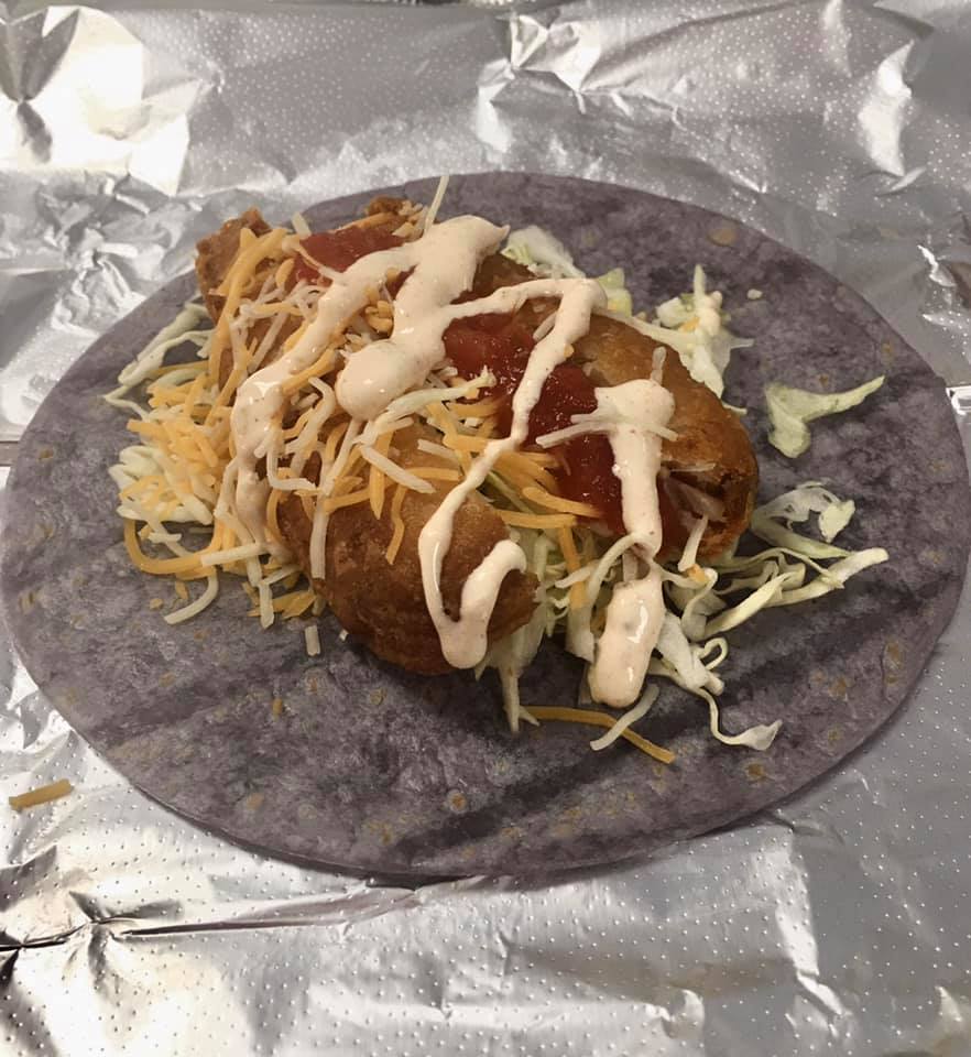 Taco on a blue tortilla, with shredded cheese, cabbage, and a sauce drizzle, on foil.
