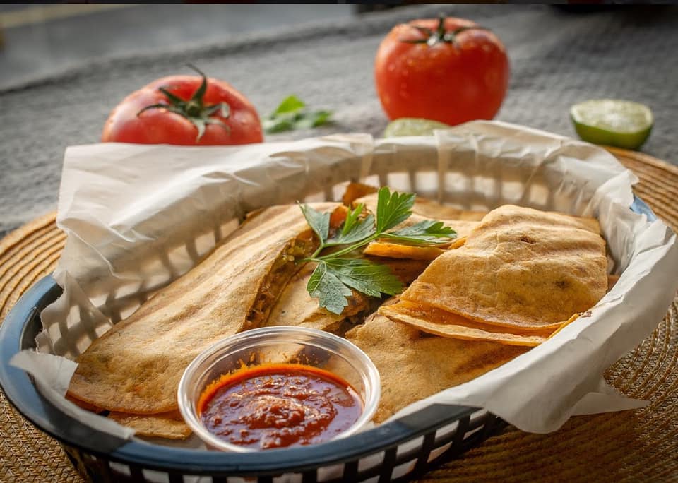 Basket of savory empanadas with red dipping sauce, tomato, and lime.