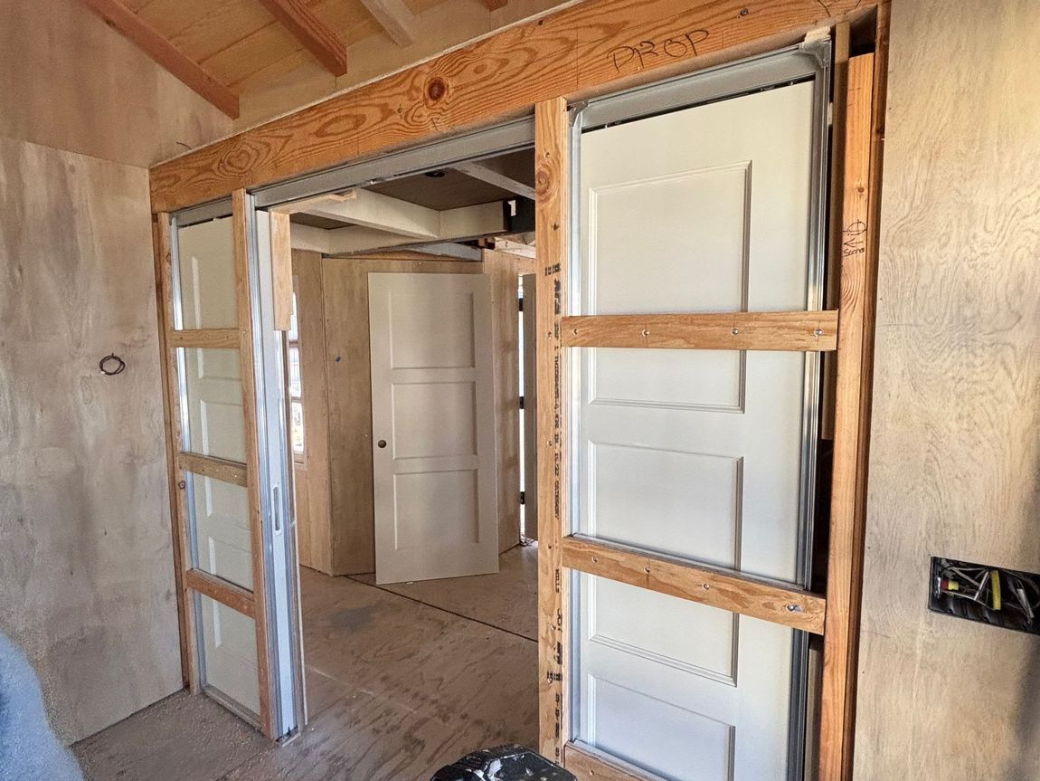 Partially framed doorway opening in an unfinished room with exposed wood studs and white paneled doors.
