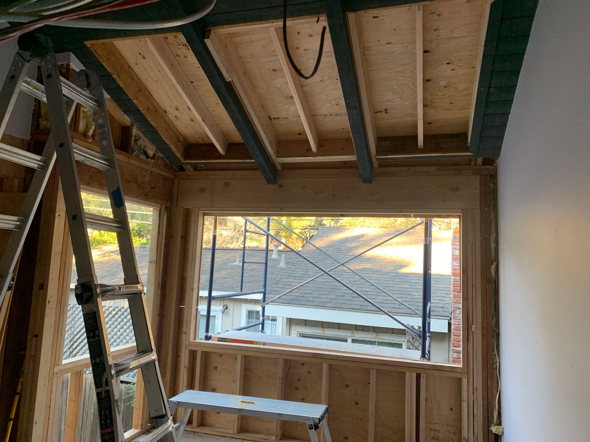 Partially finished room with exposed beams, ladder, and window opening overlooking rooftops