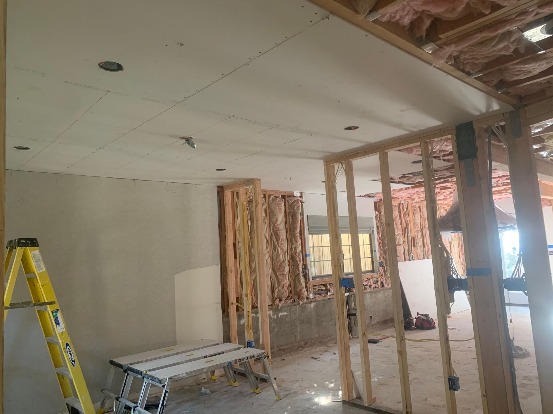 Partially demolished room with drywall framing, ladder, and construction debris under renovation