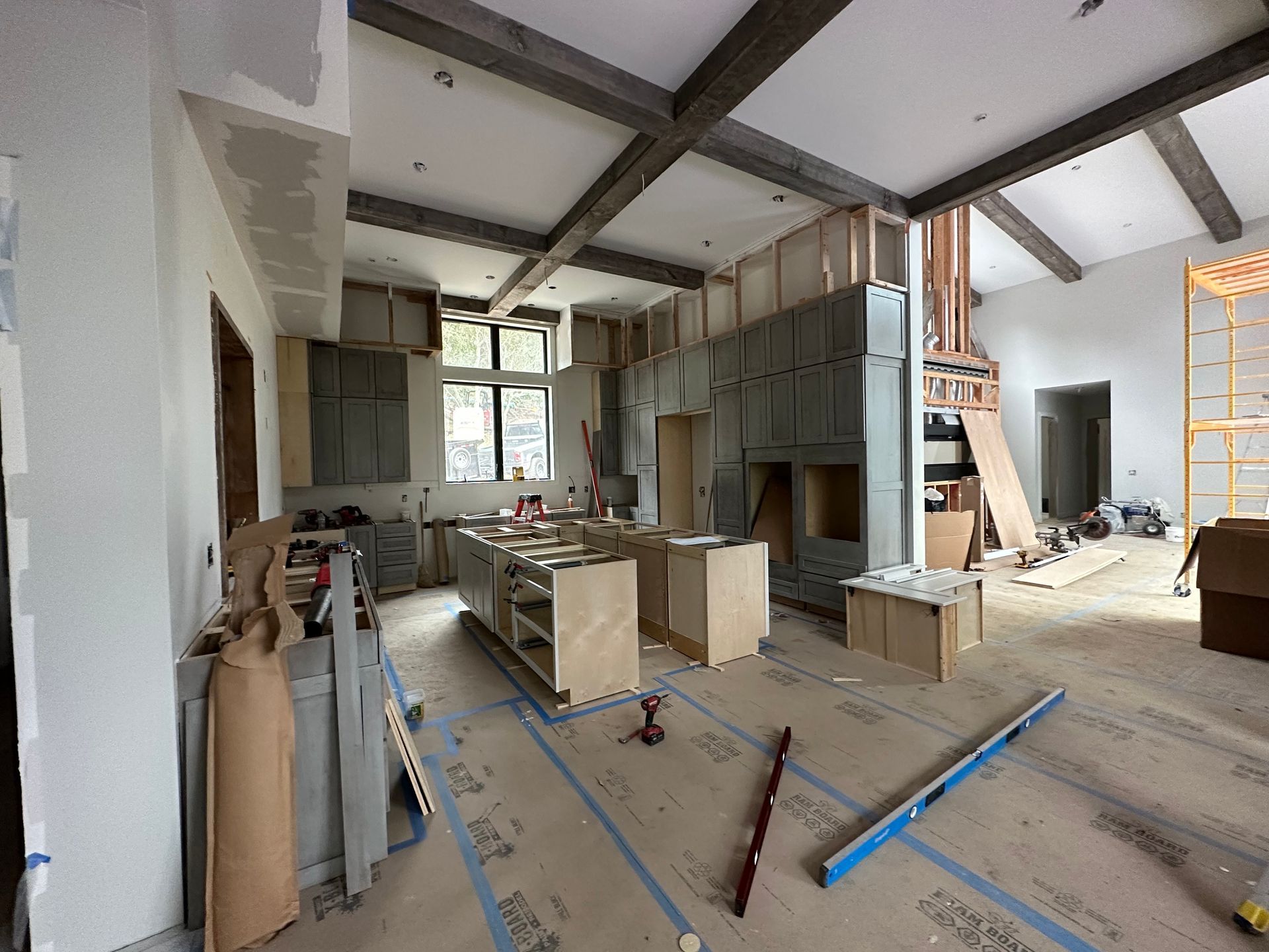 Unfinished kitchen and living space with exposed beams, cabinets, and construction tools on the floor