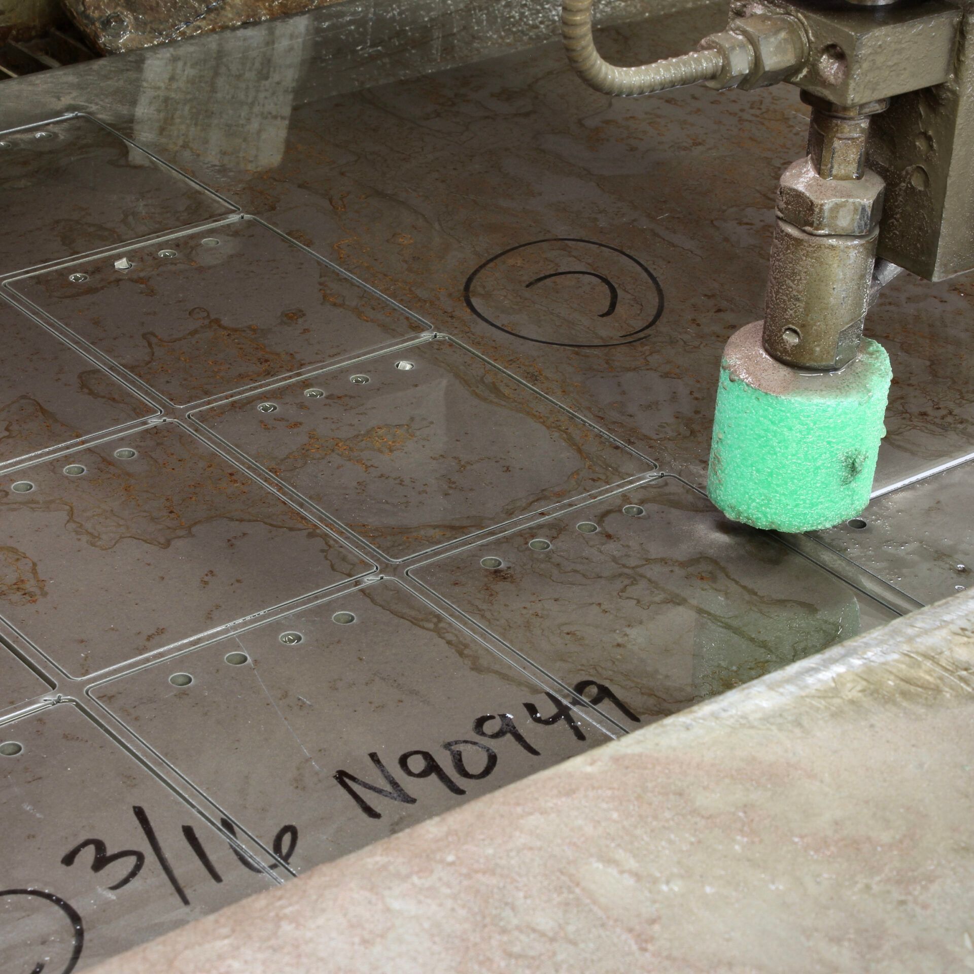 Wet metal floor with pipes and a green foam-covered fixture, marked with handwritten black numbers.