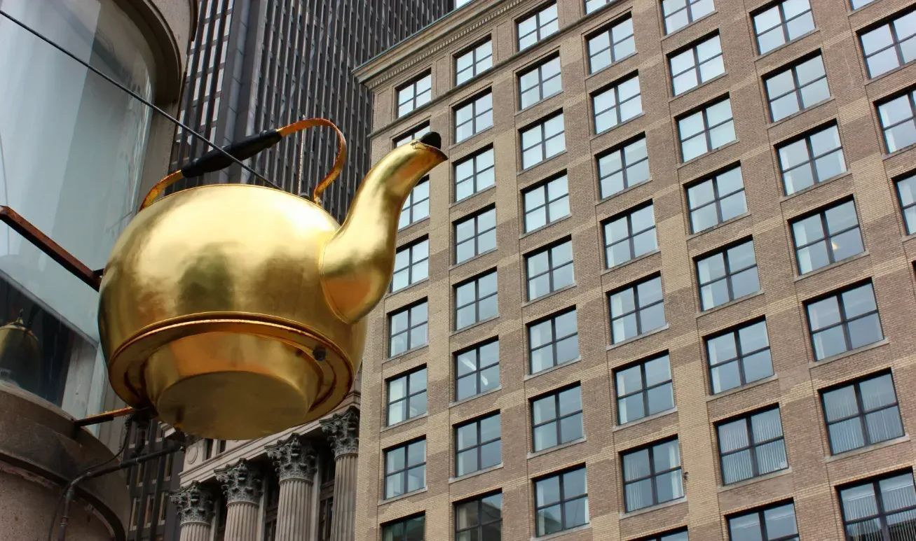 Golden teapot sculpture mounted on a building exterior beside tall office windows