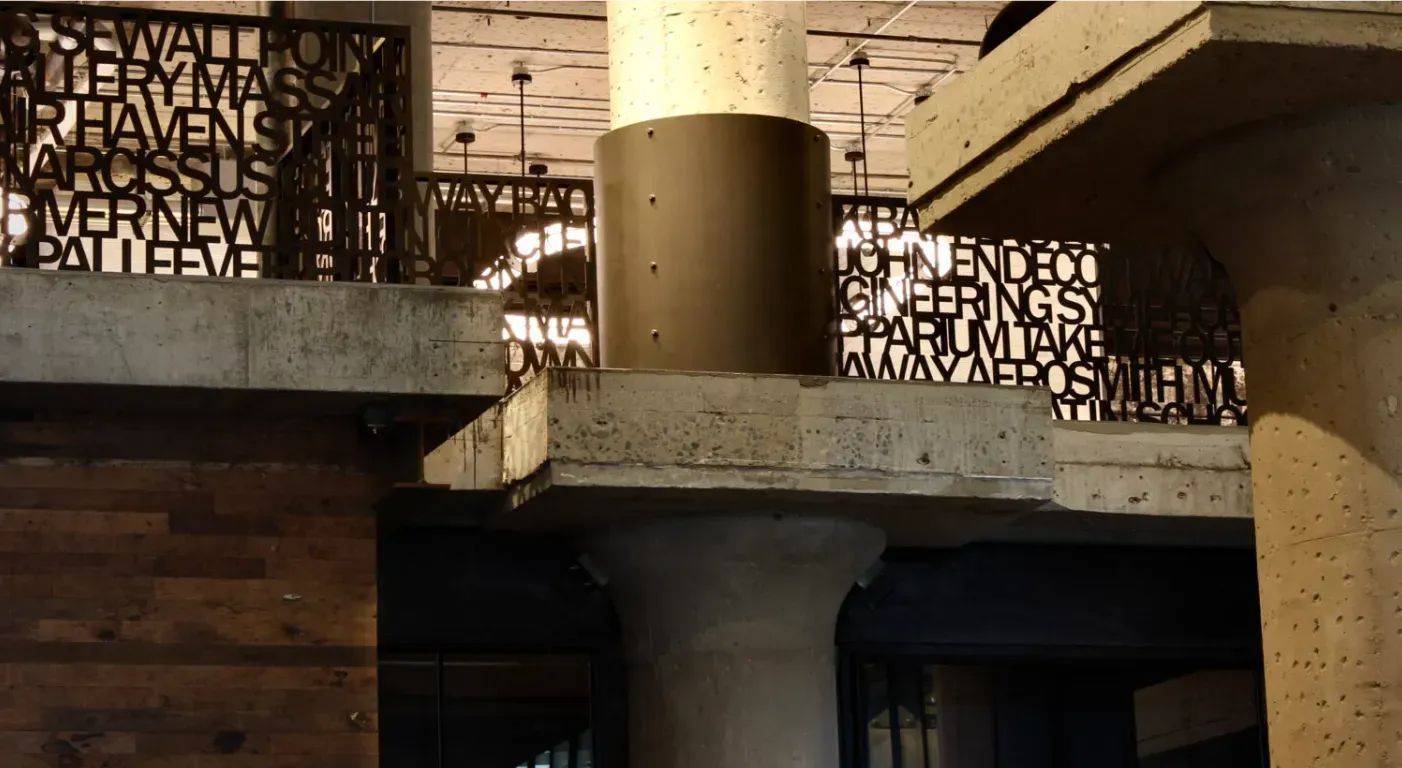 Indoor architectural scene with wood paneling, concrete columns, and decorative metal railings in warm light
