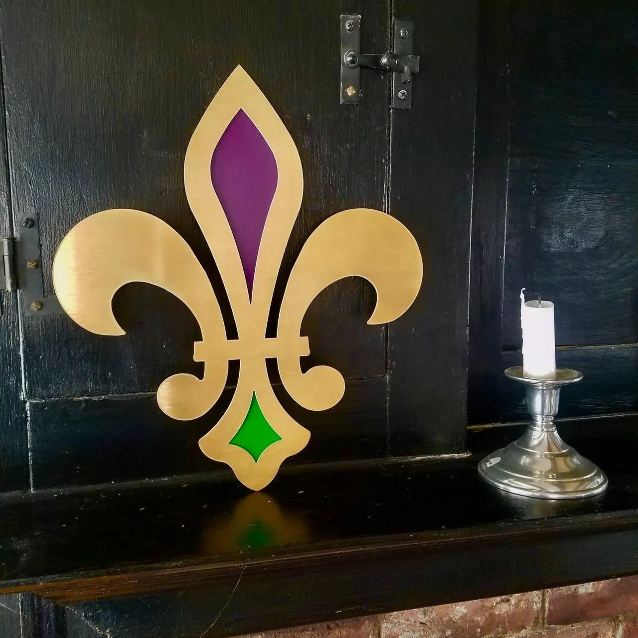 Gold fleur-de-lis decoration with purple and green accents on a dark cabinet beside a candle holder