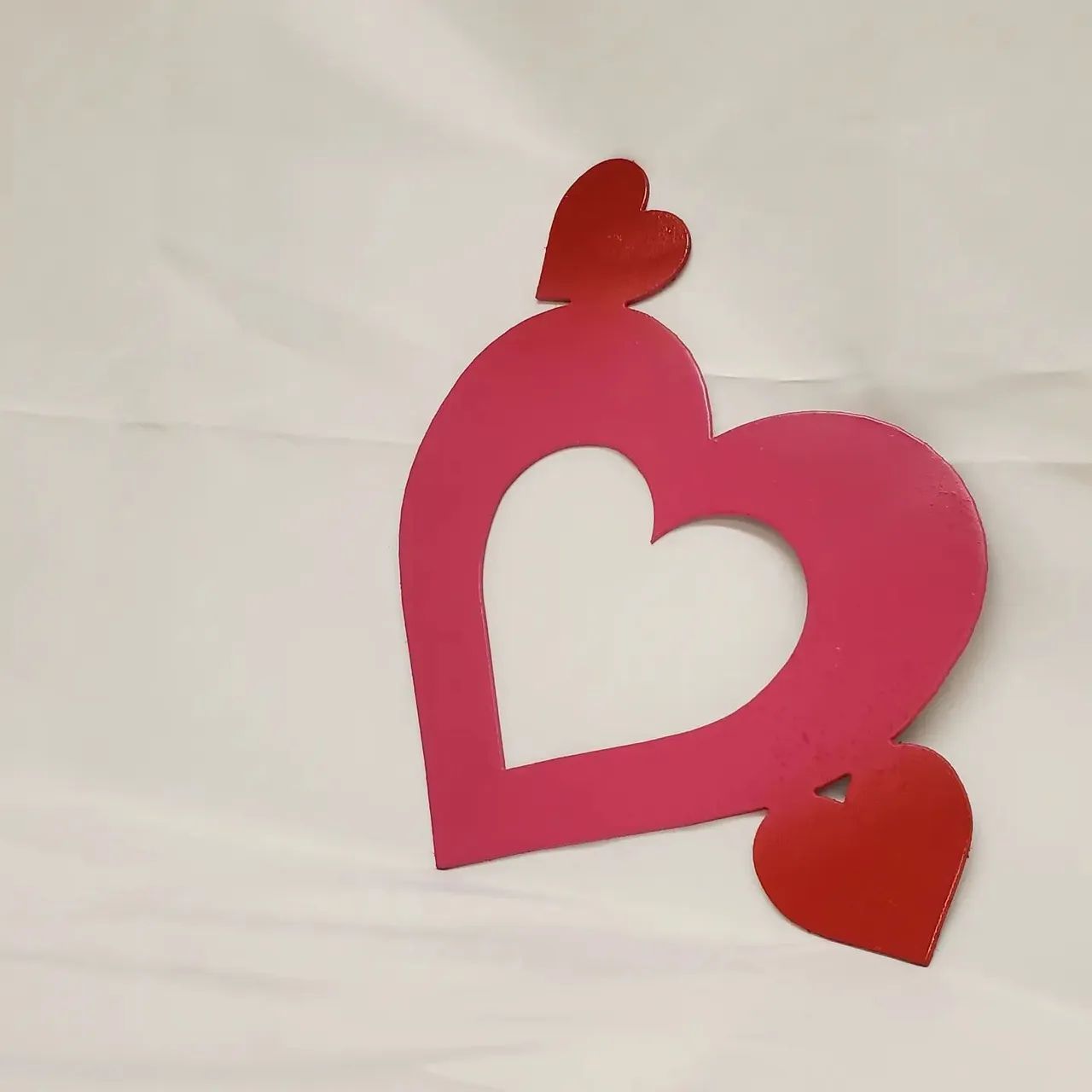Pink heart-shaped paper cutout with two small red hearts on a white background