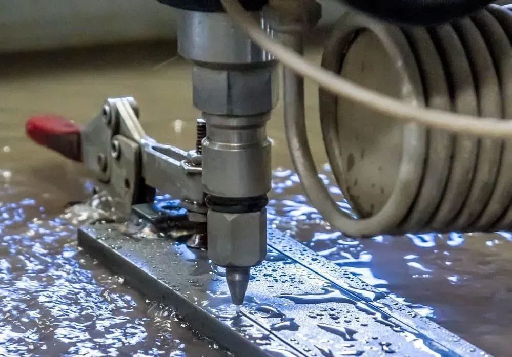 A CNC machine tool cutting a metal plate with coolant splashing around it.