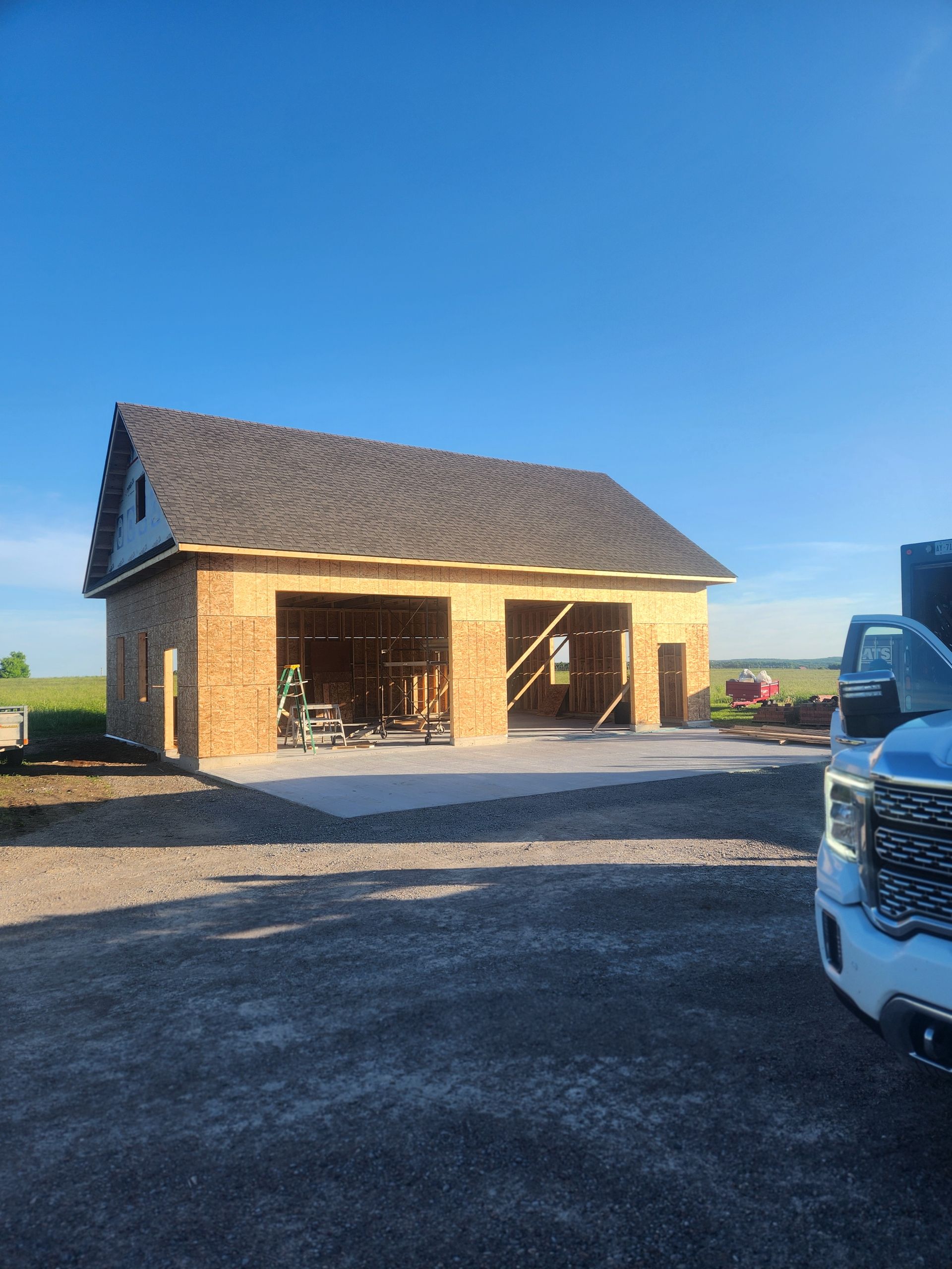 Small brick garage under construction on a gravel lot, with a blue truck partially visible at right.