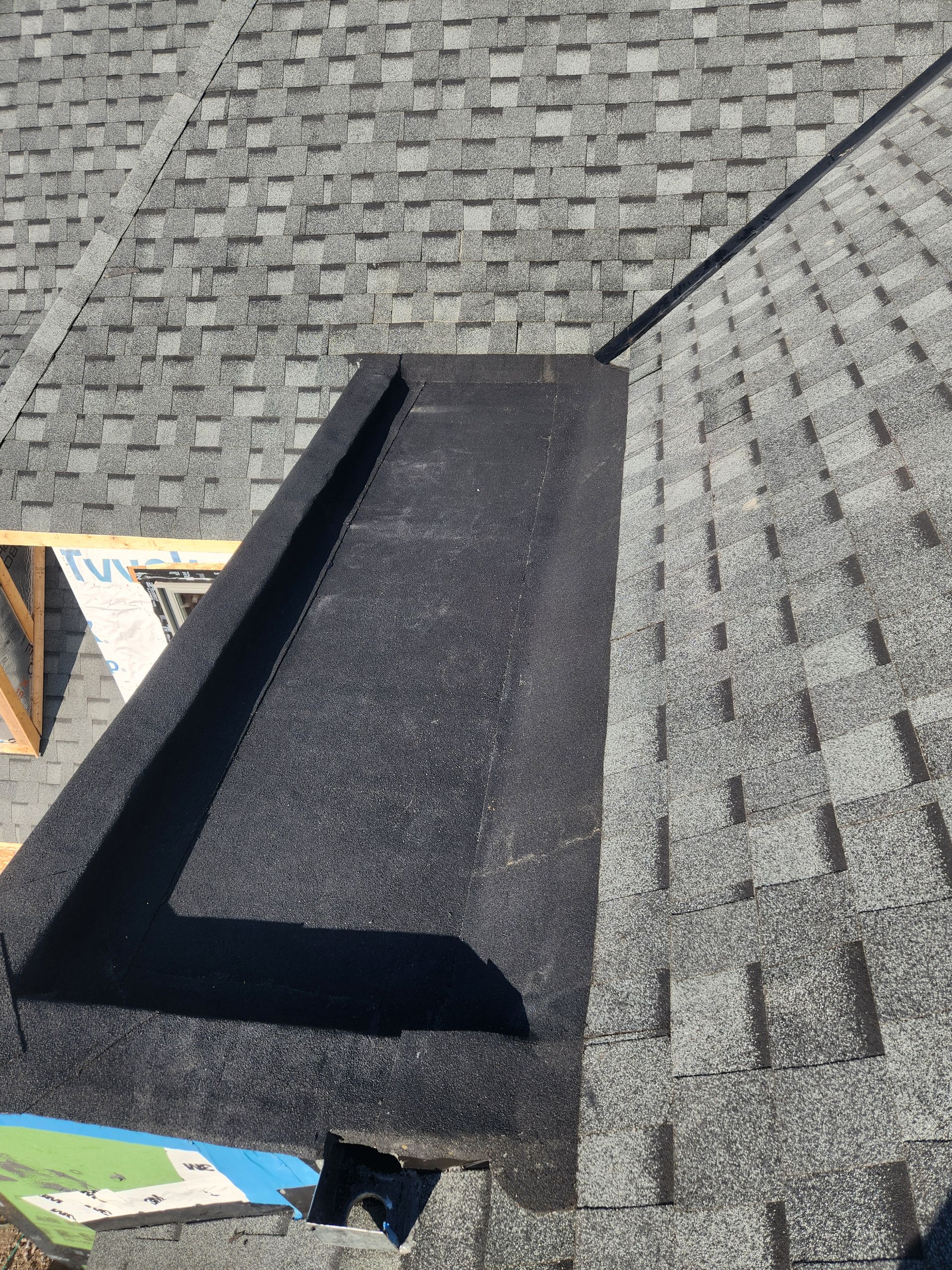 Black roof vent on a gray shingled roof under a bright sky.