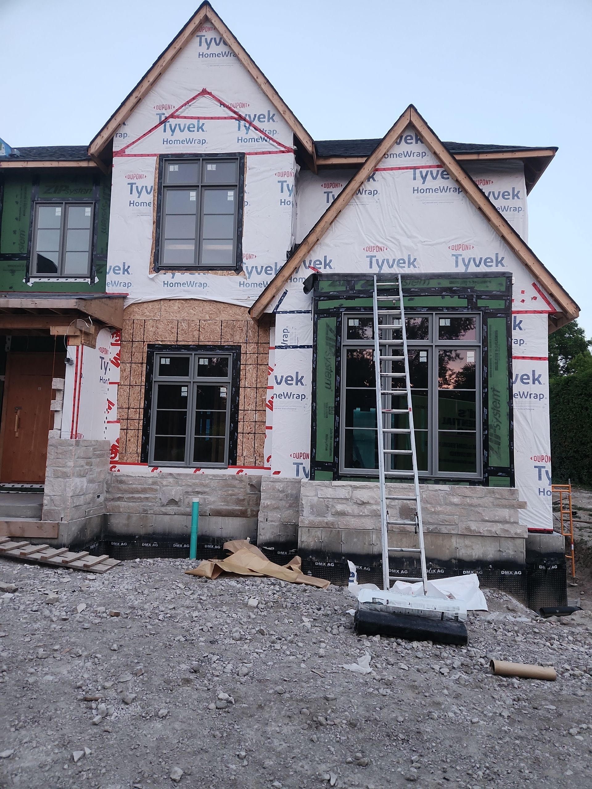 Partially built two-story house with exposed Tyvek wrap, windows, and gravel front yard