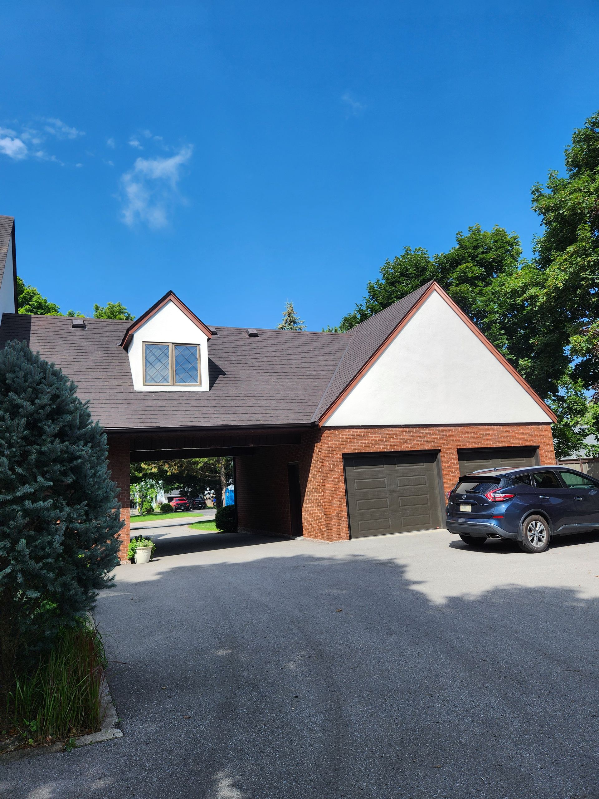 Brick house with a dark roof, garage, gravel driveway, and parked SUV under a blue sky