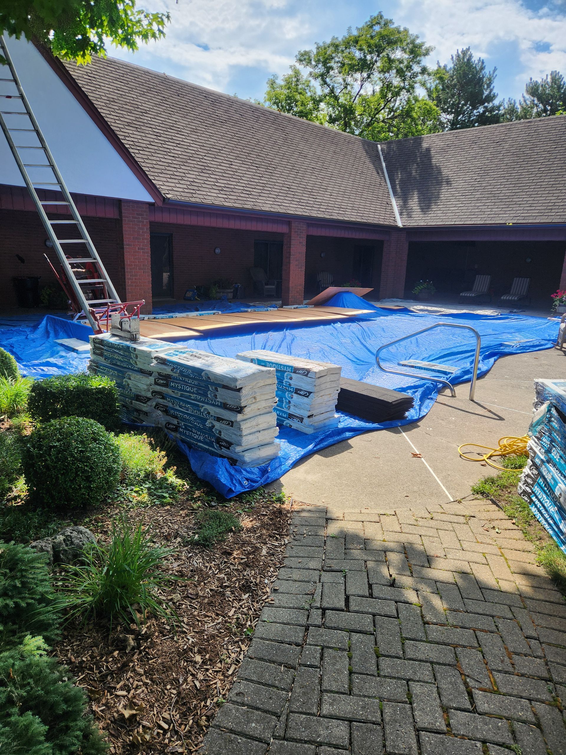 Courtyard with stacked blue-tarped materials, ladders, and a curved tiled roof under construction