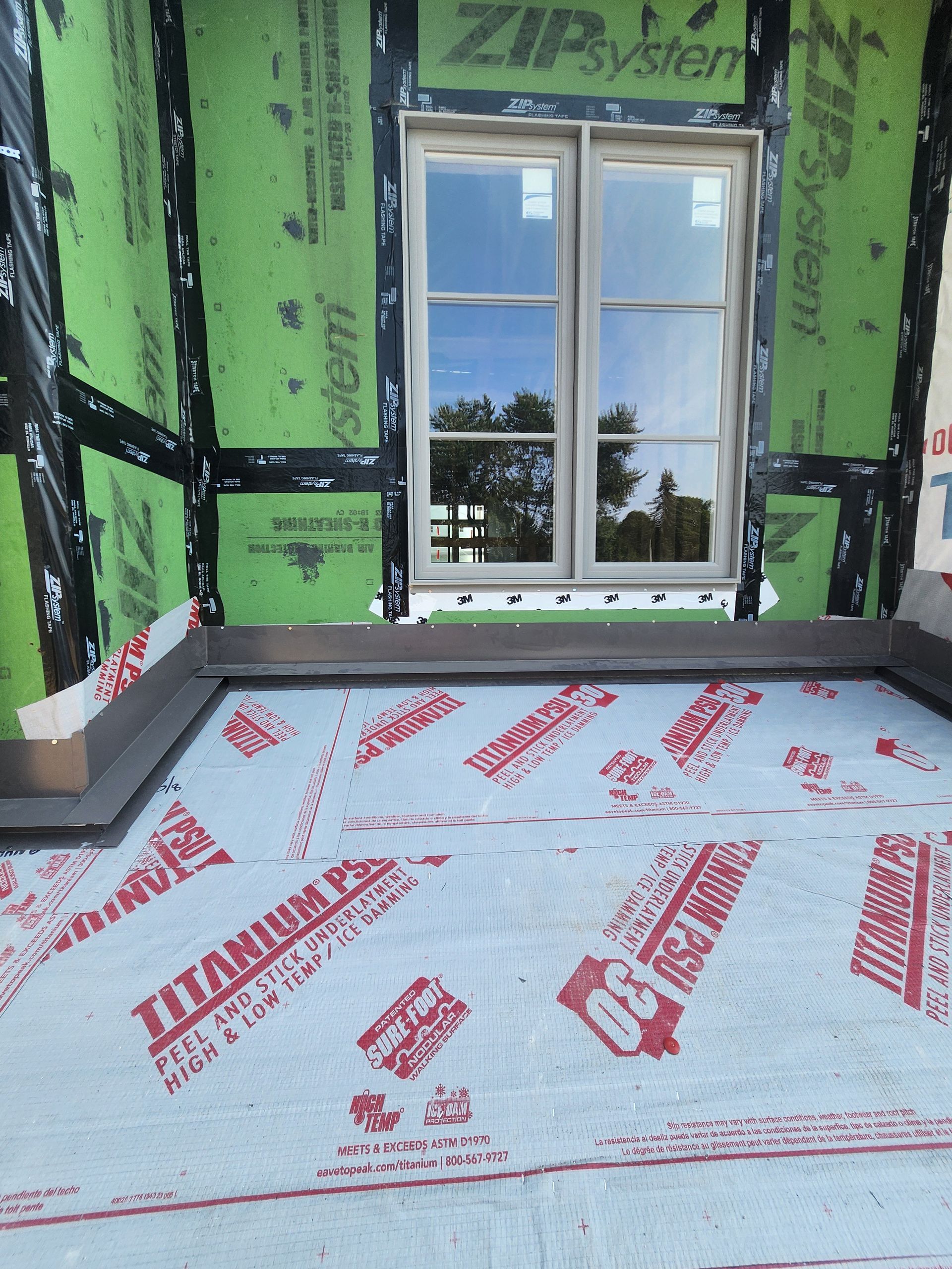 Unfinished room with green insulated walls, window, and floor covered in red-labeled protective sheeting