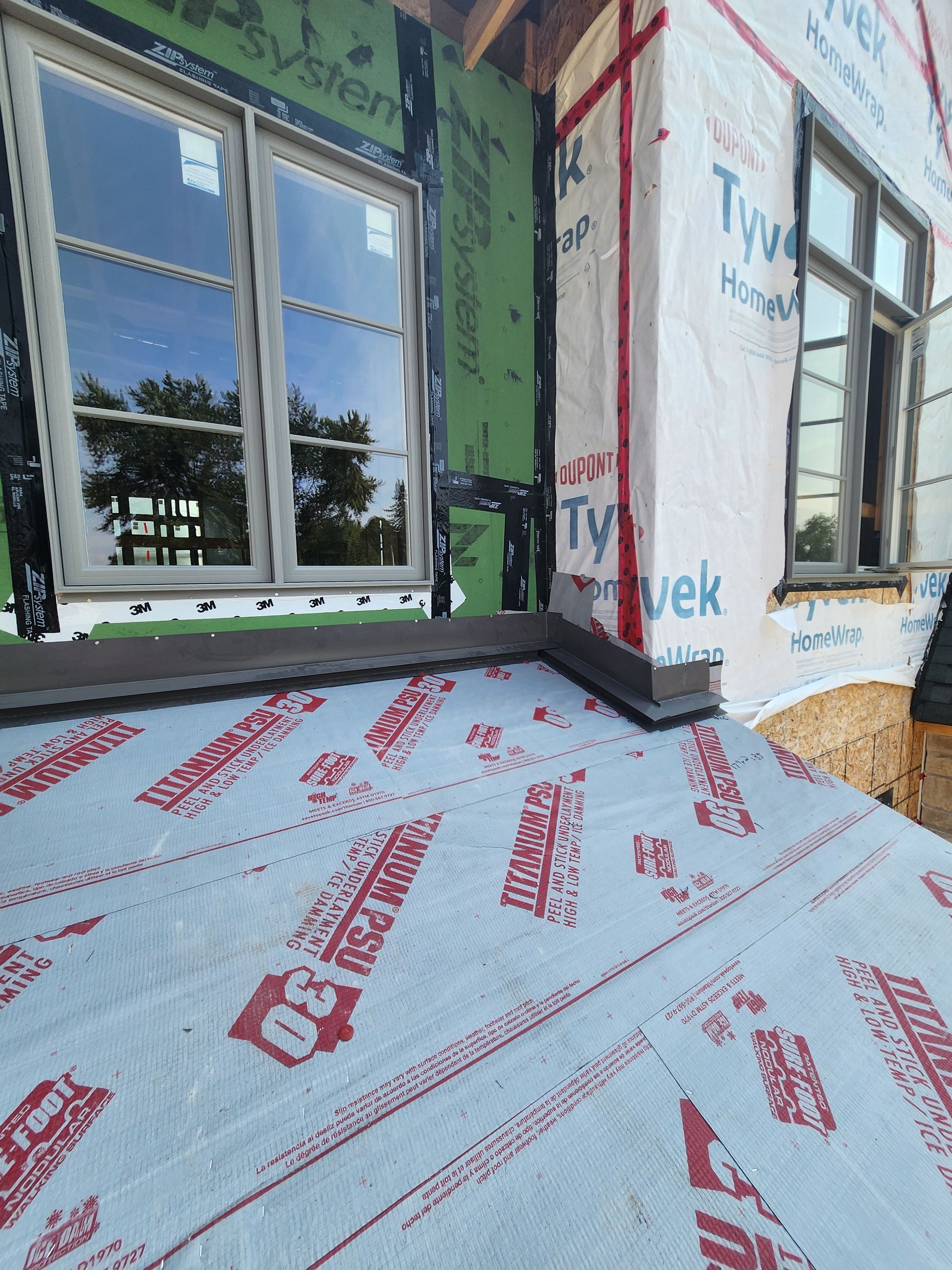 House exterior under construction with white Tyvek wrap, green sheathing, and a window on the wall