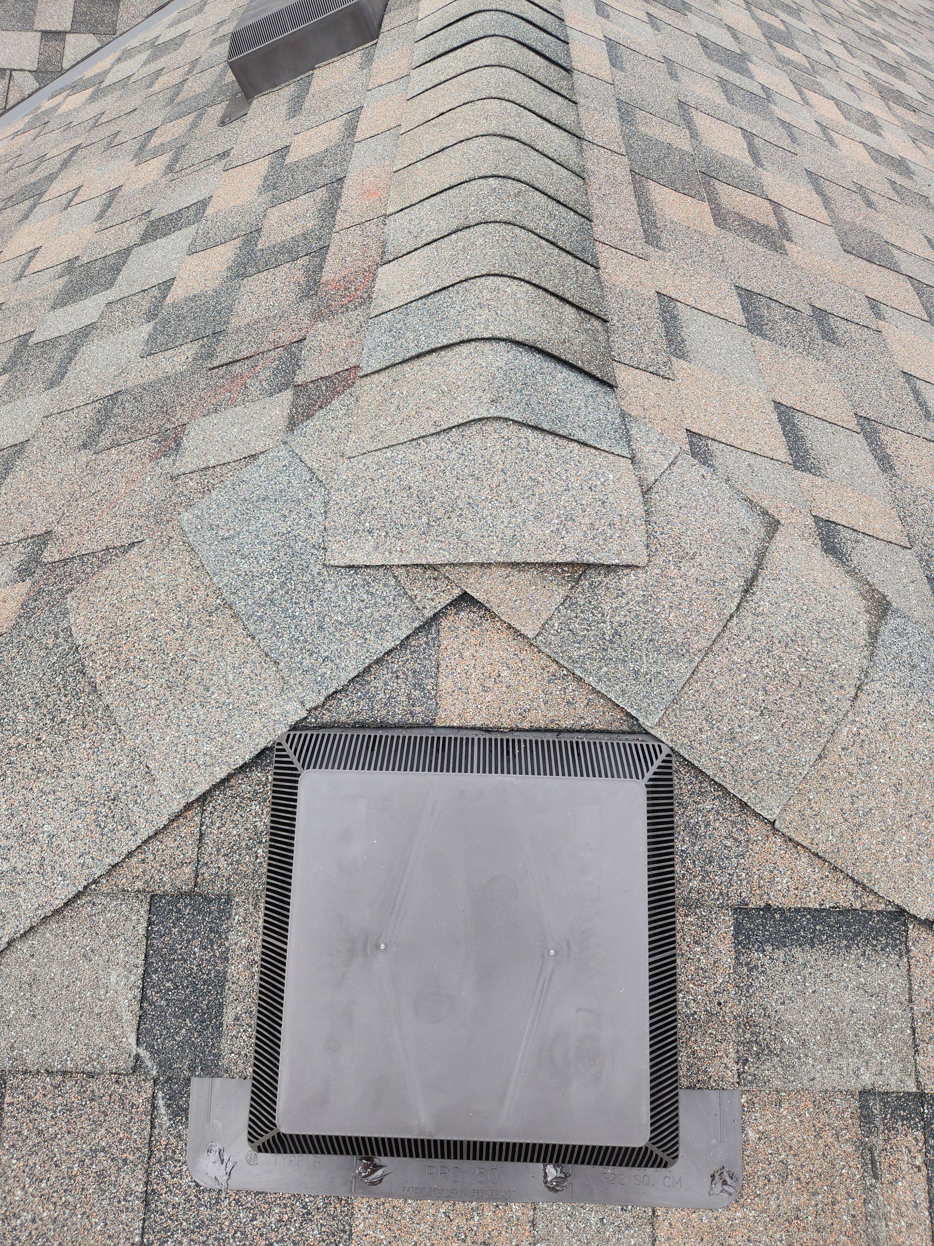 Roof shingles with a metal vent or skylight opening near the bottom center.