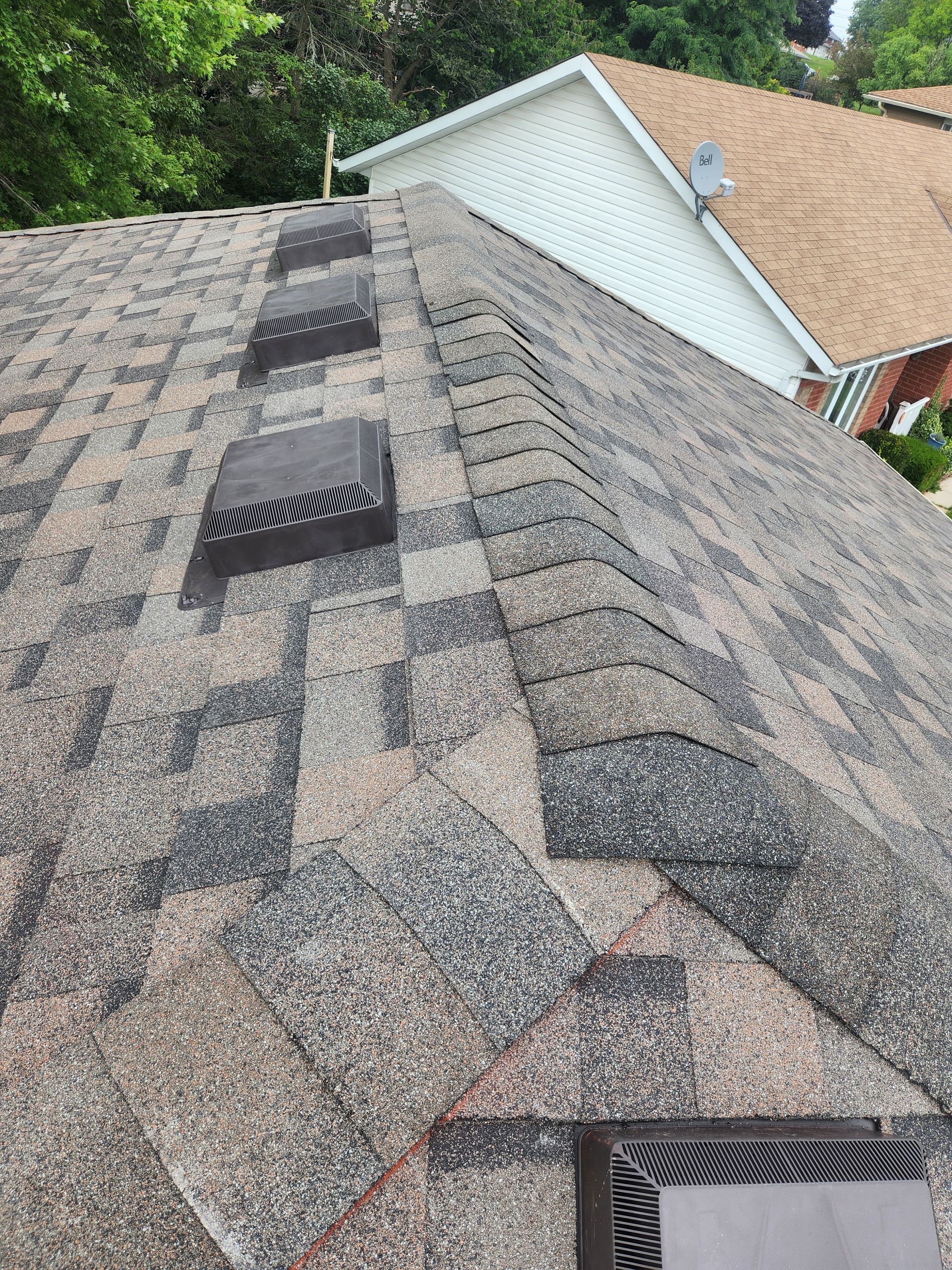 Close-up of a shingled roof with several dark roof vents and a neighboring house visible