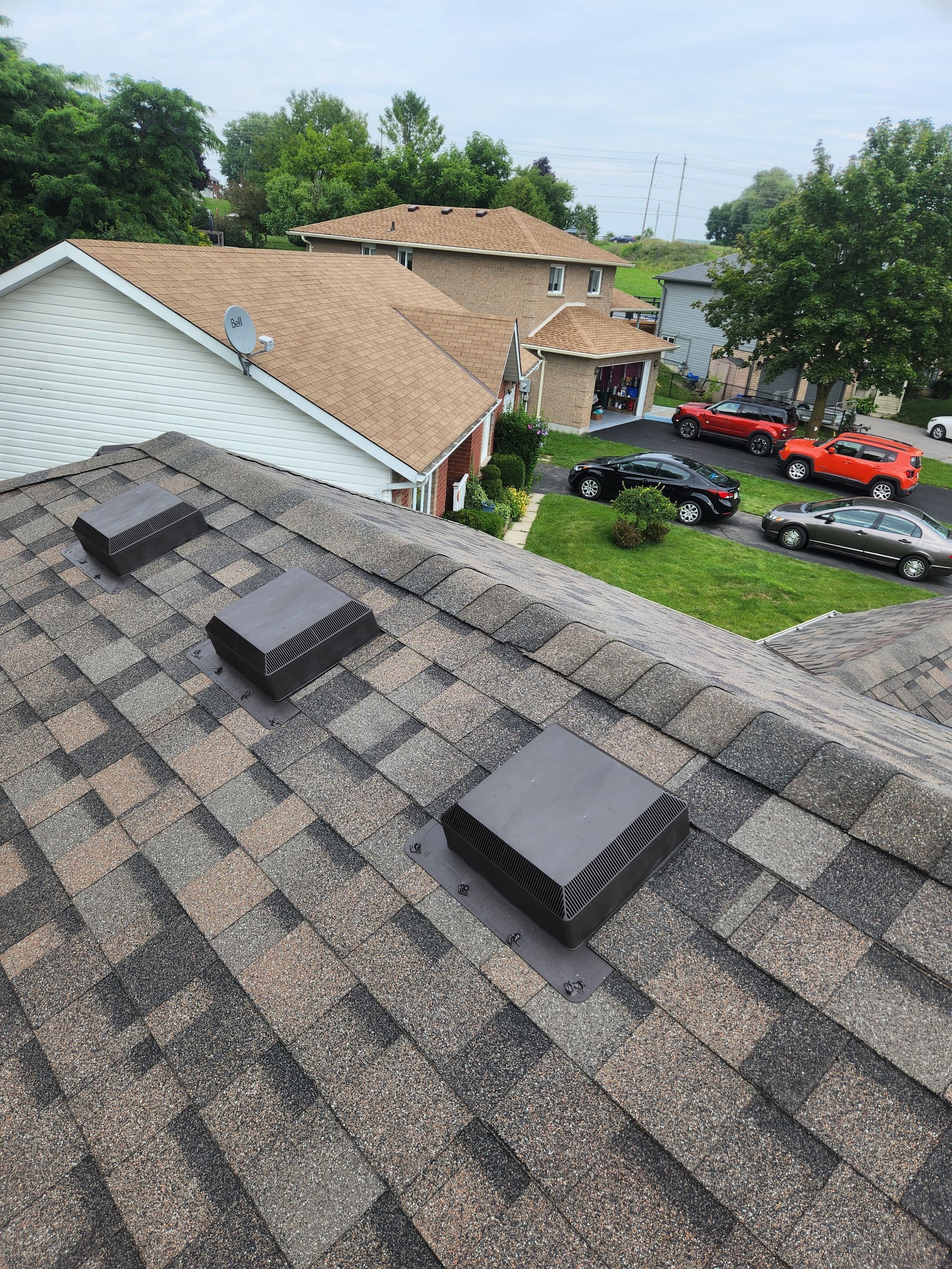 Rooftop view with gray shingles, vent stacks, and parked red cars near houses and trees