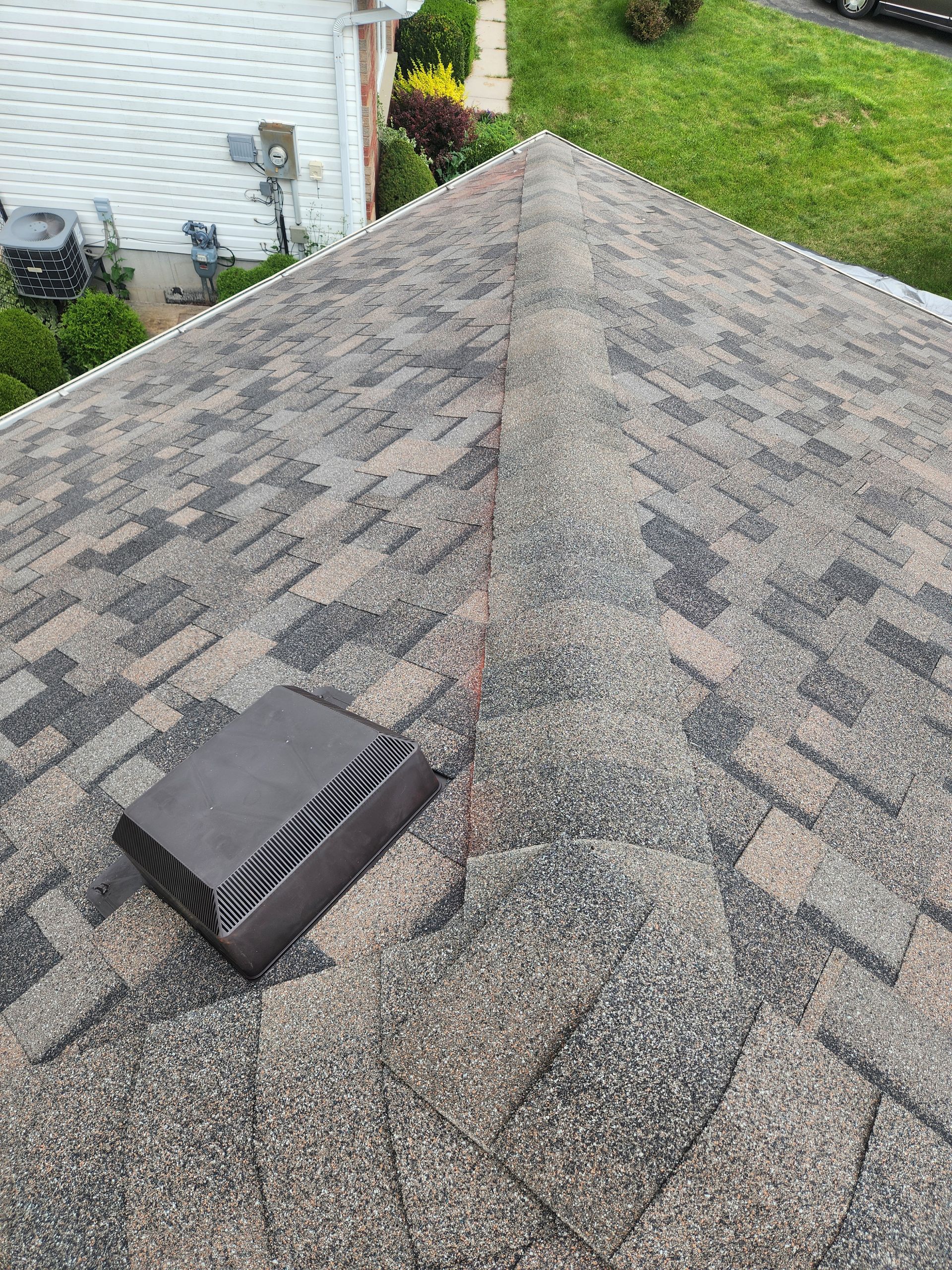 Roof with gray asphalt shingles and a small black vent near the ridge, beside a white house wall.