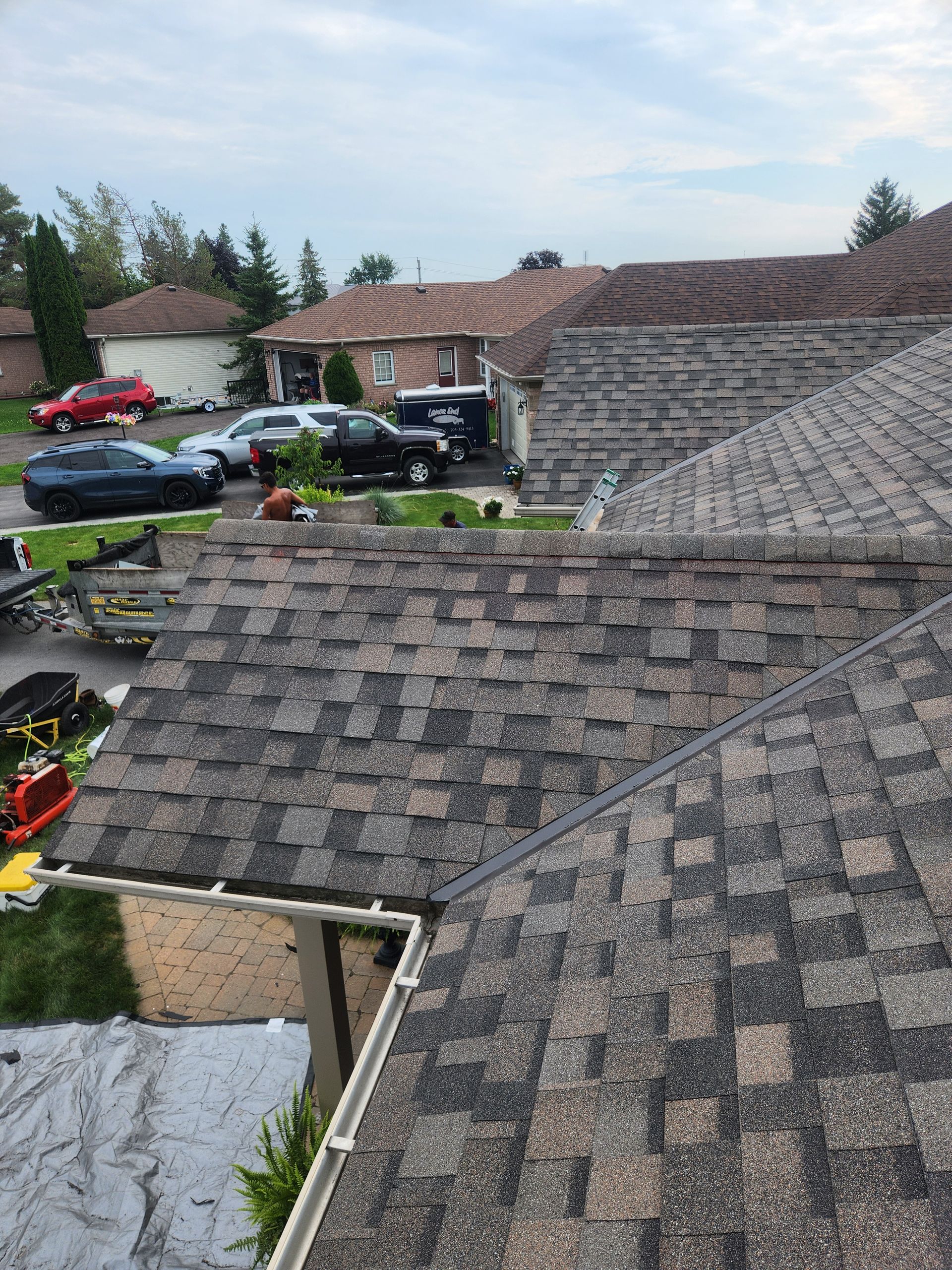Suburban houses with gray shingle roofs and parked cars on a rainy day