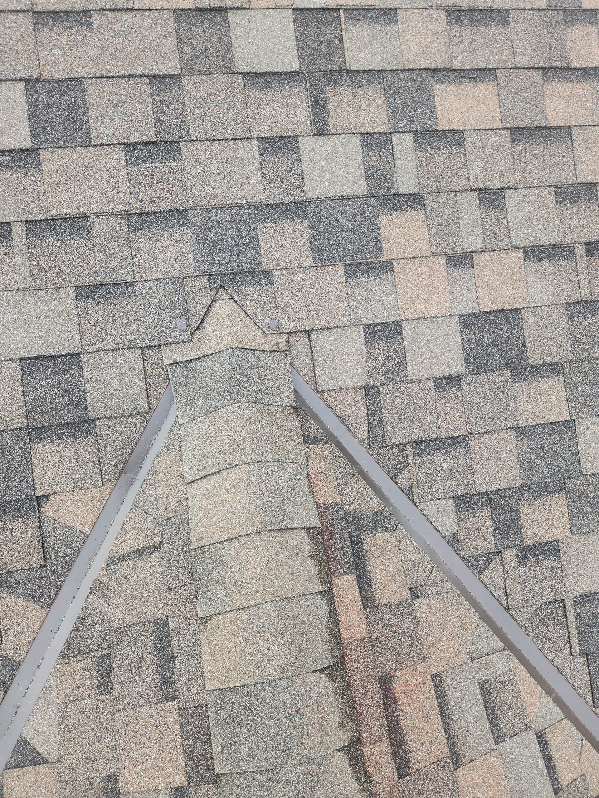 Rooftop shingles with two metal rails leading toward a small damaged spot near the center.