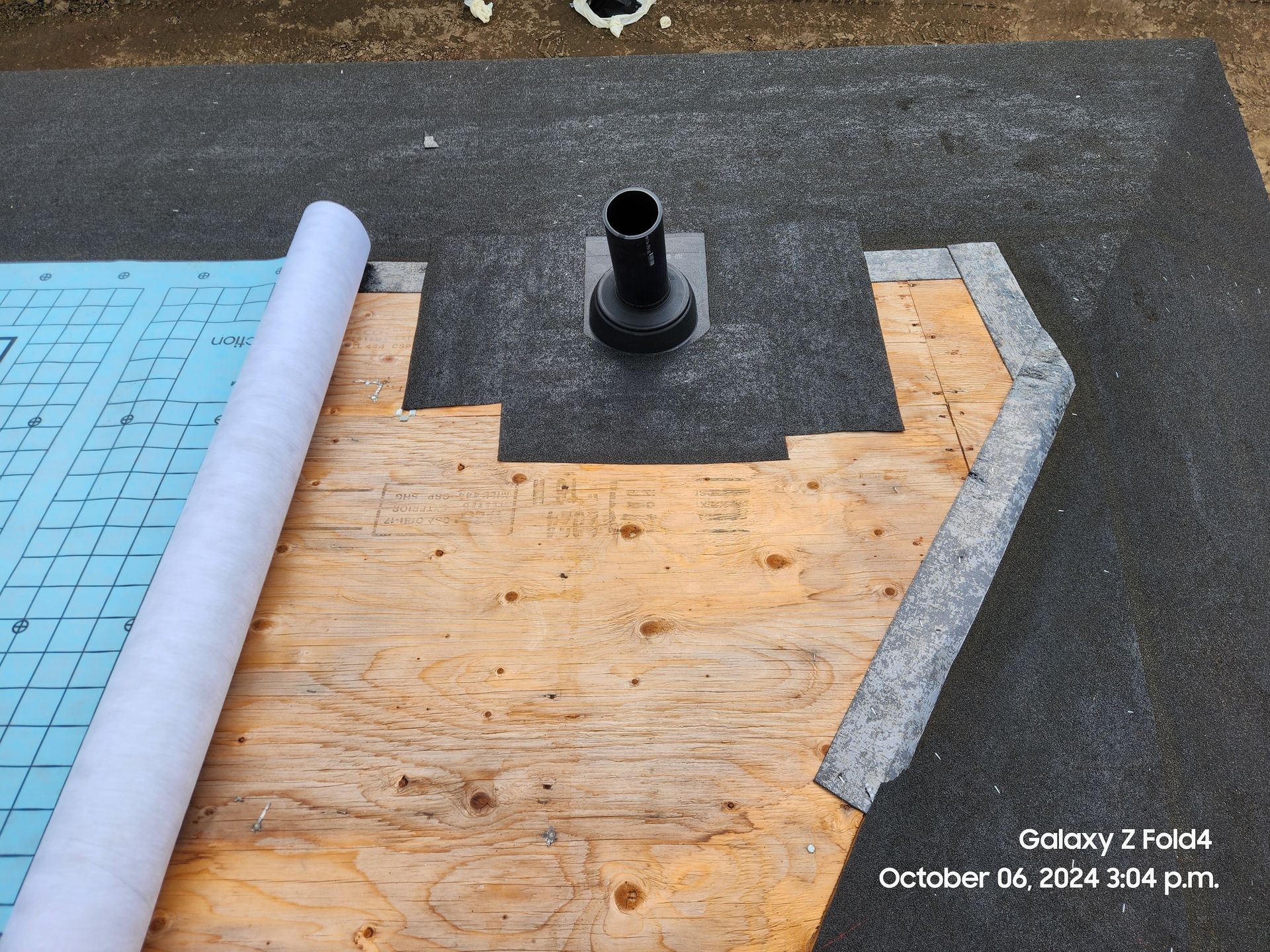Roof repair with wood decking, black underlayment, gray roll, and a vent pipe opening