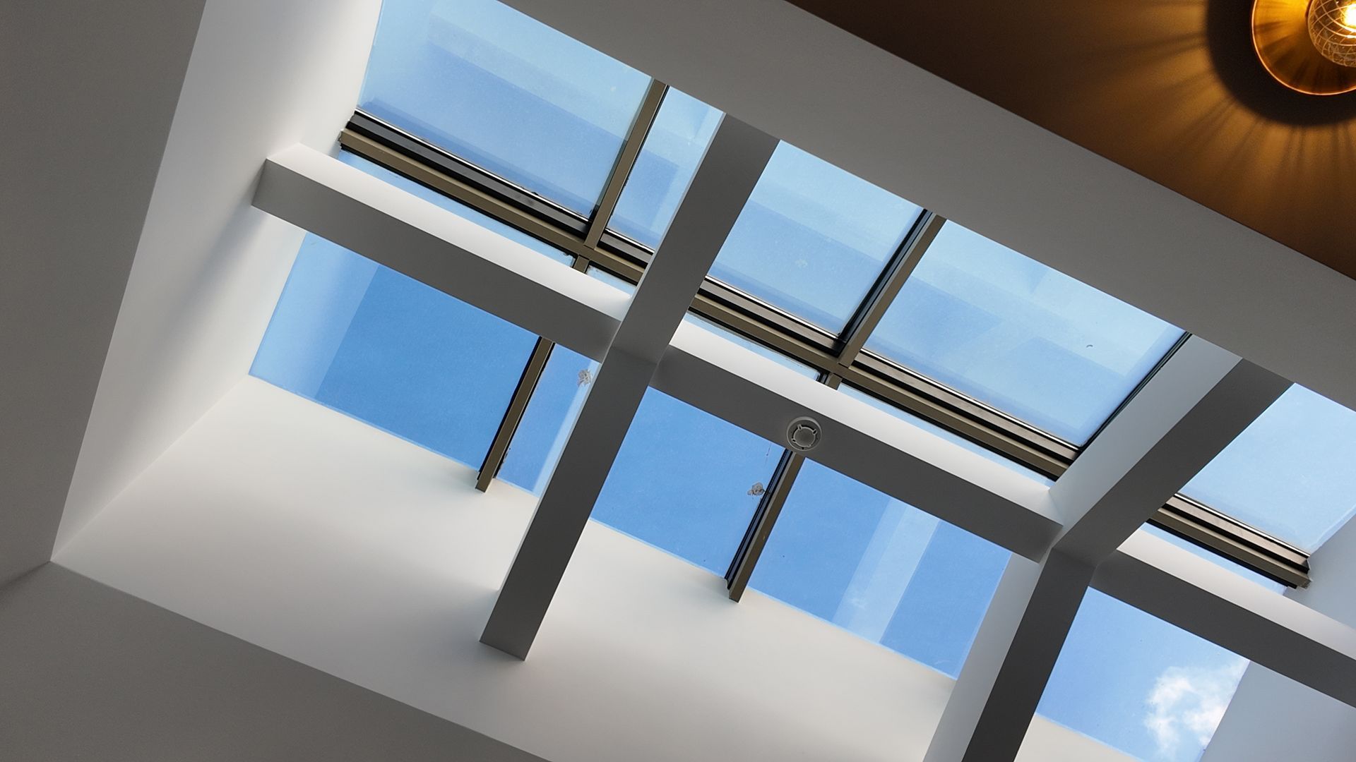 Modern skylight ceiling with white beams and blue sky visible through glass panels