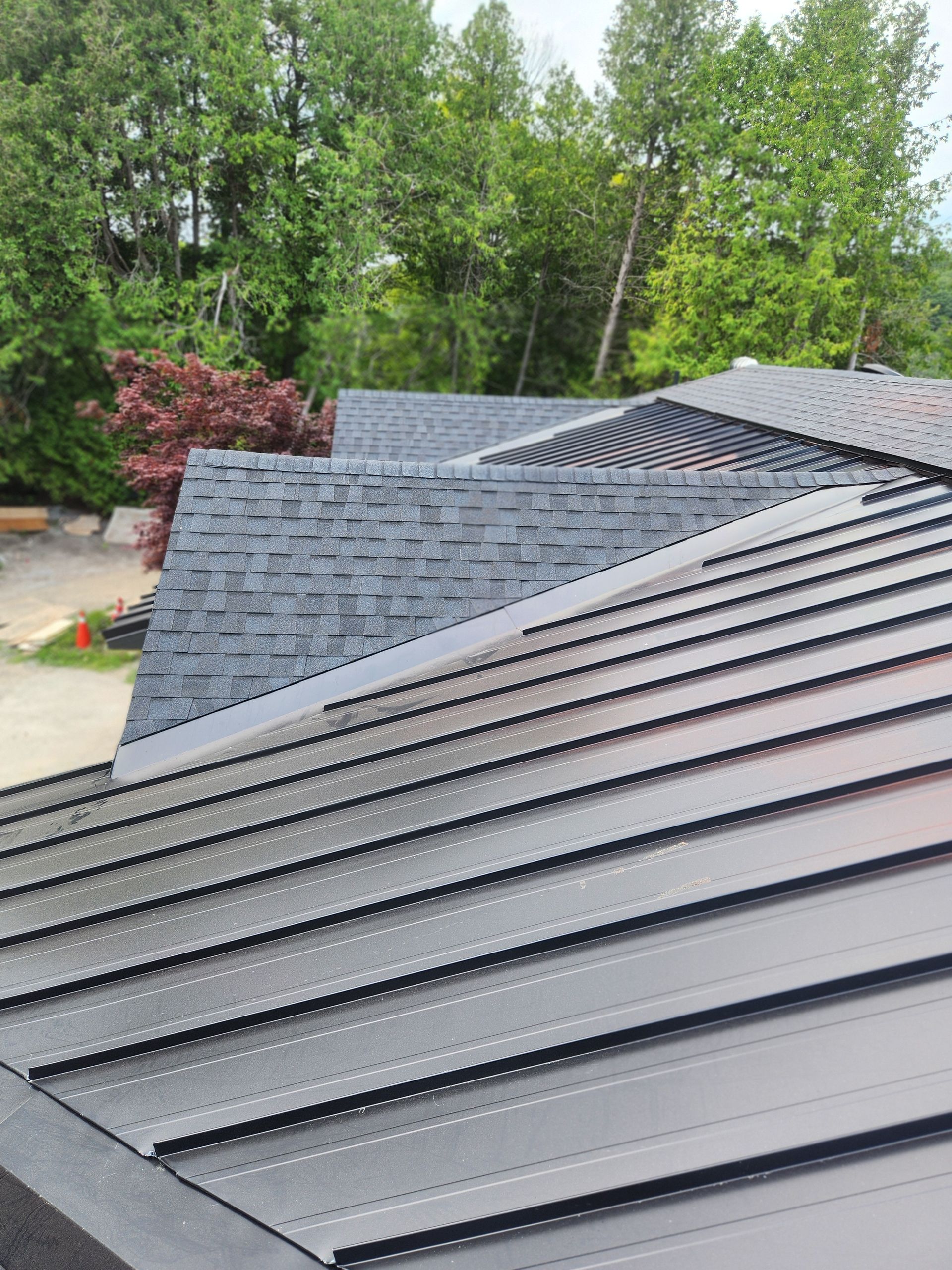 Close-up of a dark gray shingle roof with green trees in the background