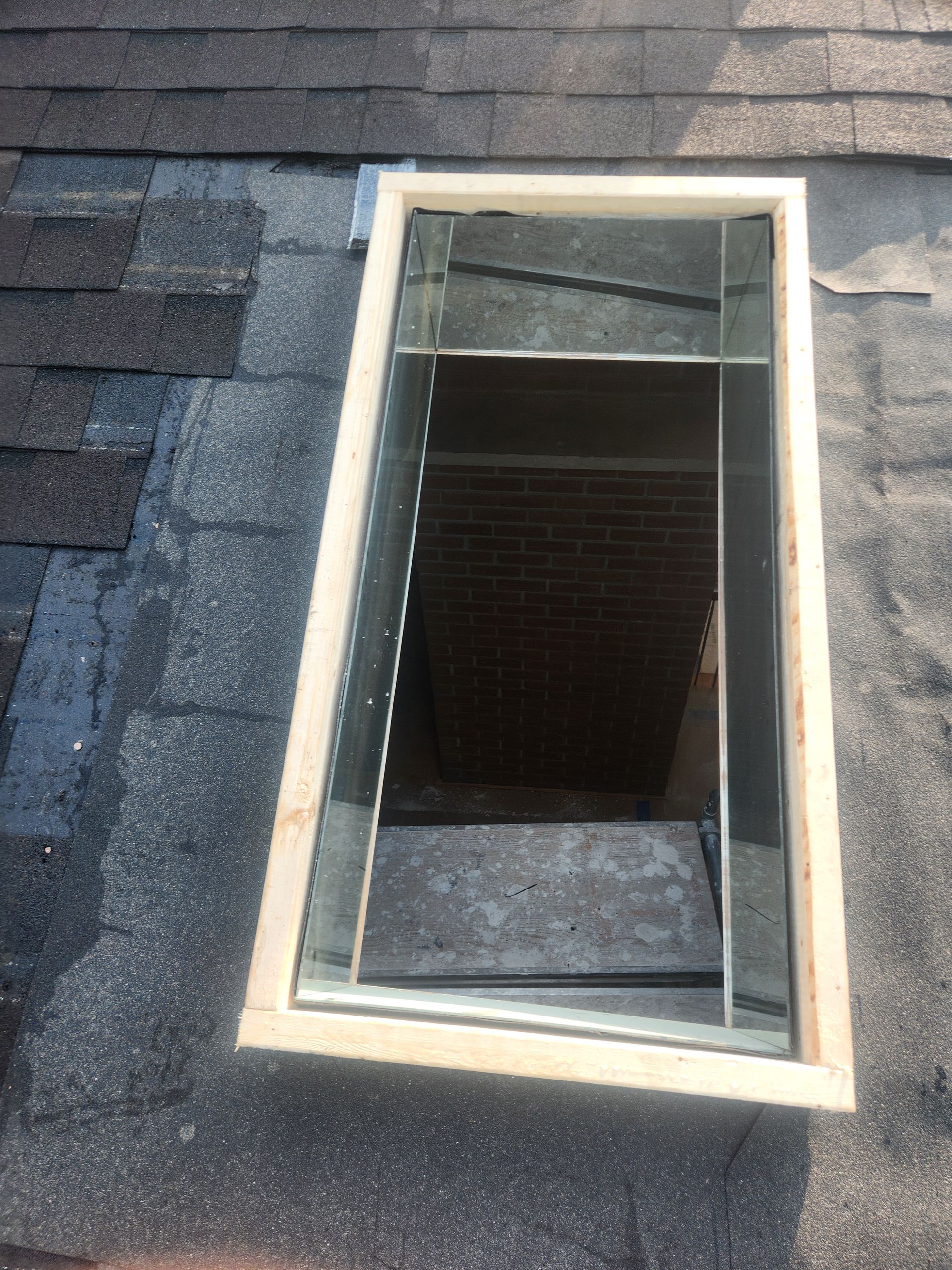 Open rooftop skylight with a beige frame in a dark shingled roof