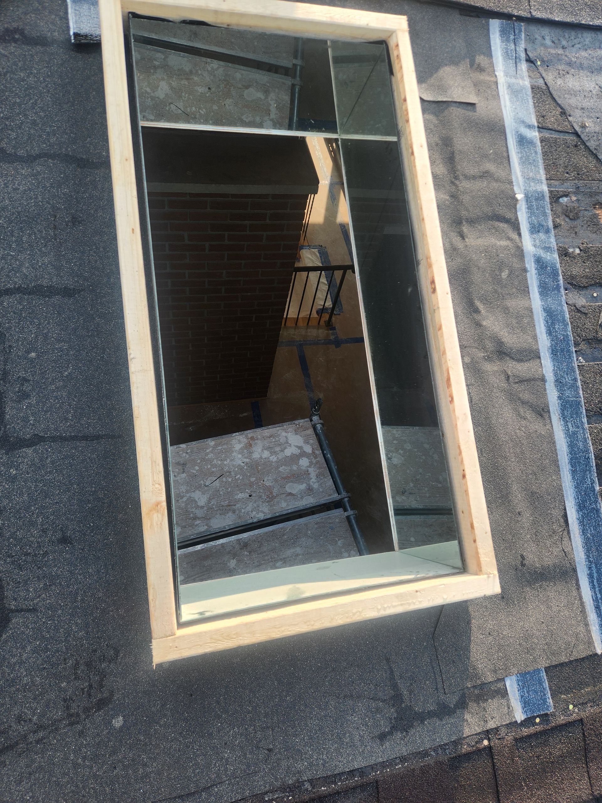 Open roof window with beige trim set in dark gray shingles, showing a loft interior inside.
