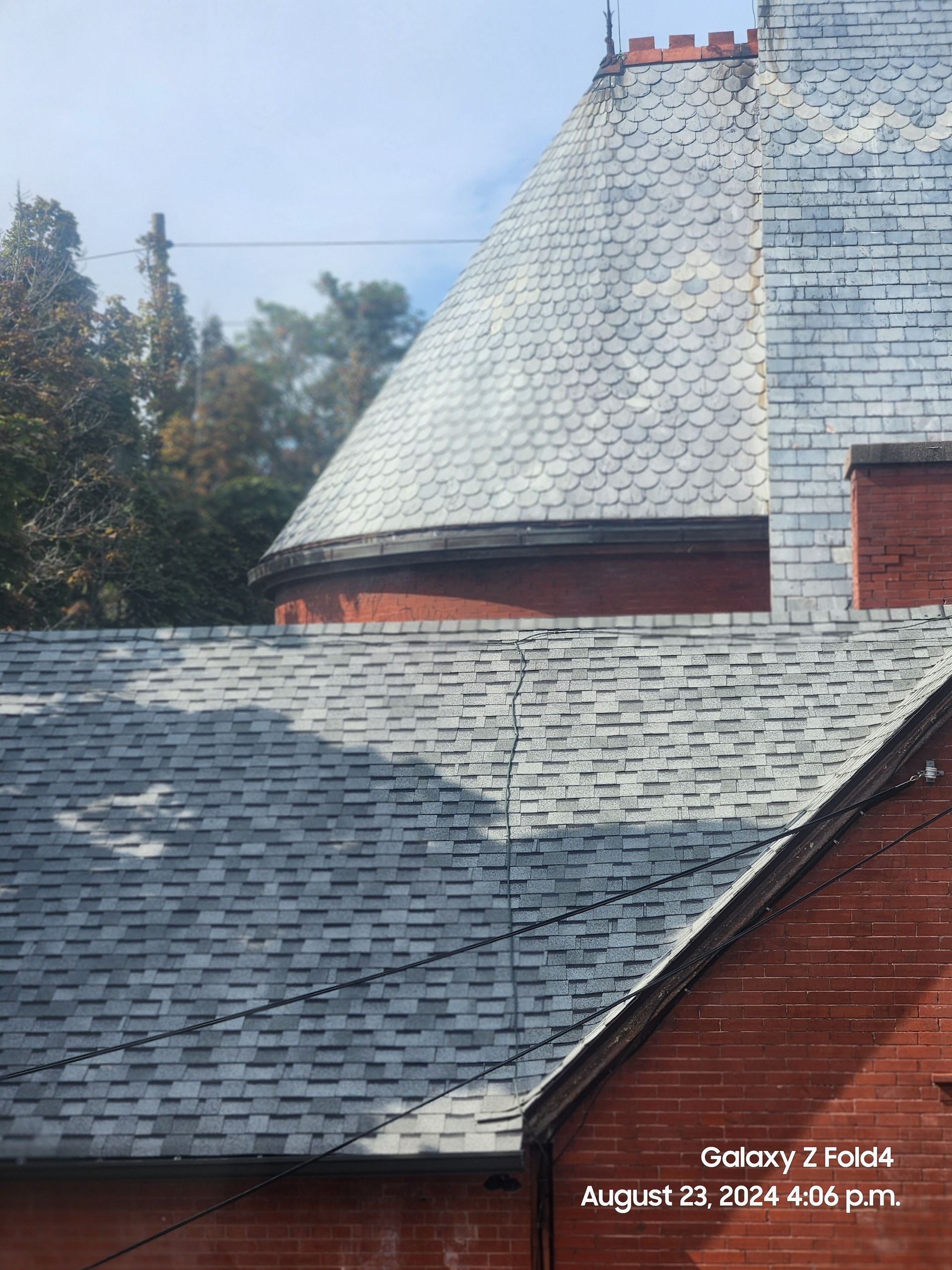 Slate-roofed house with a steep conical turret and trees in the background